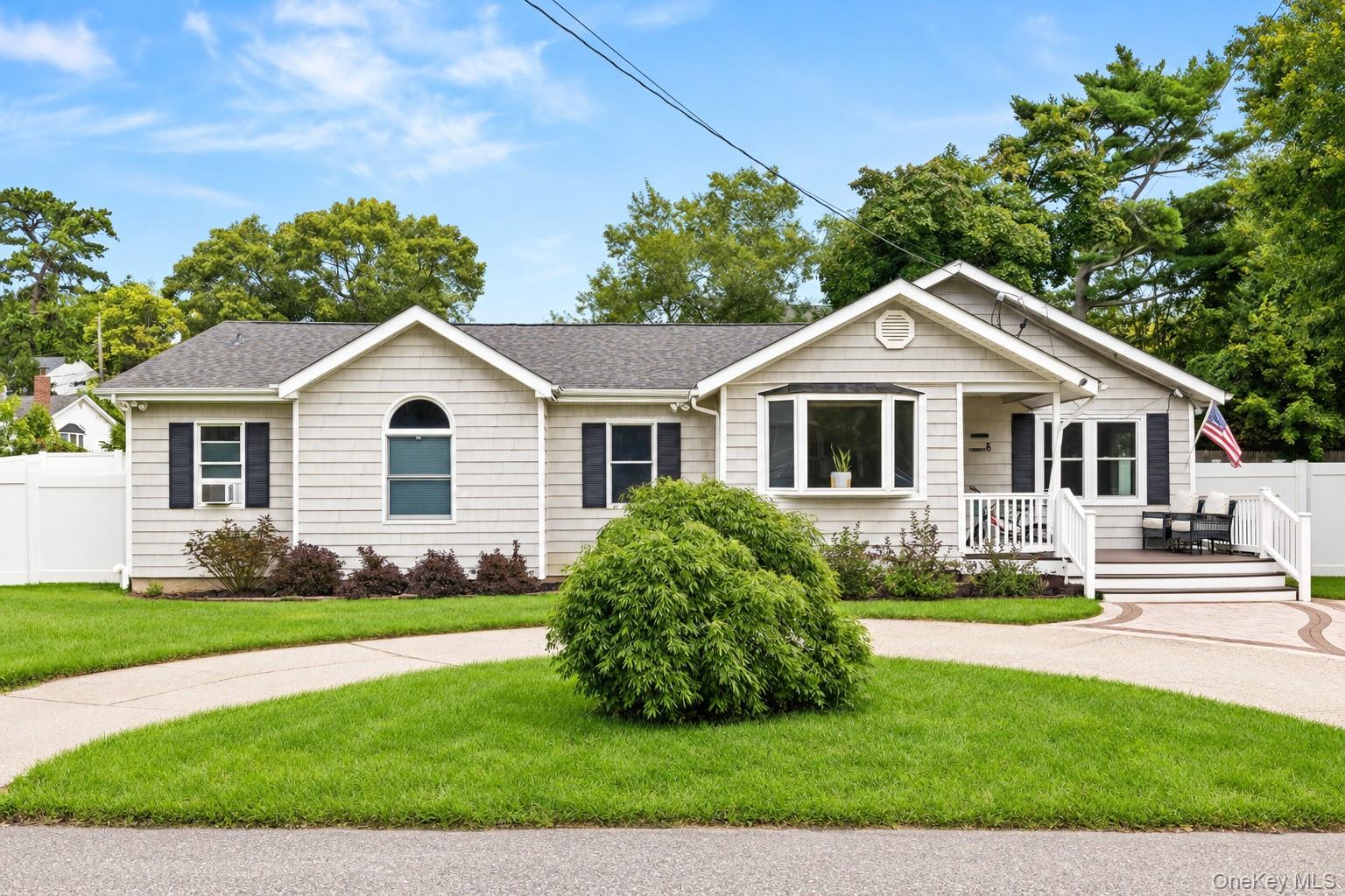 Single-story light-sided home with a covered porch, American flag, and curved driveway.