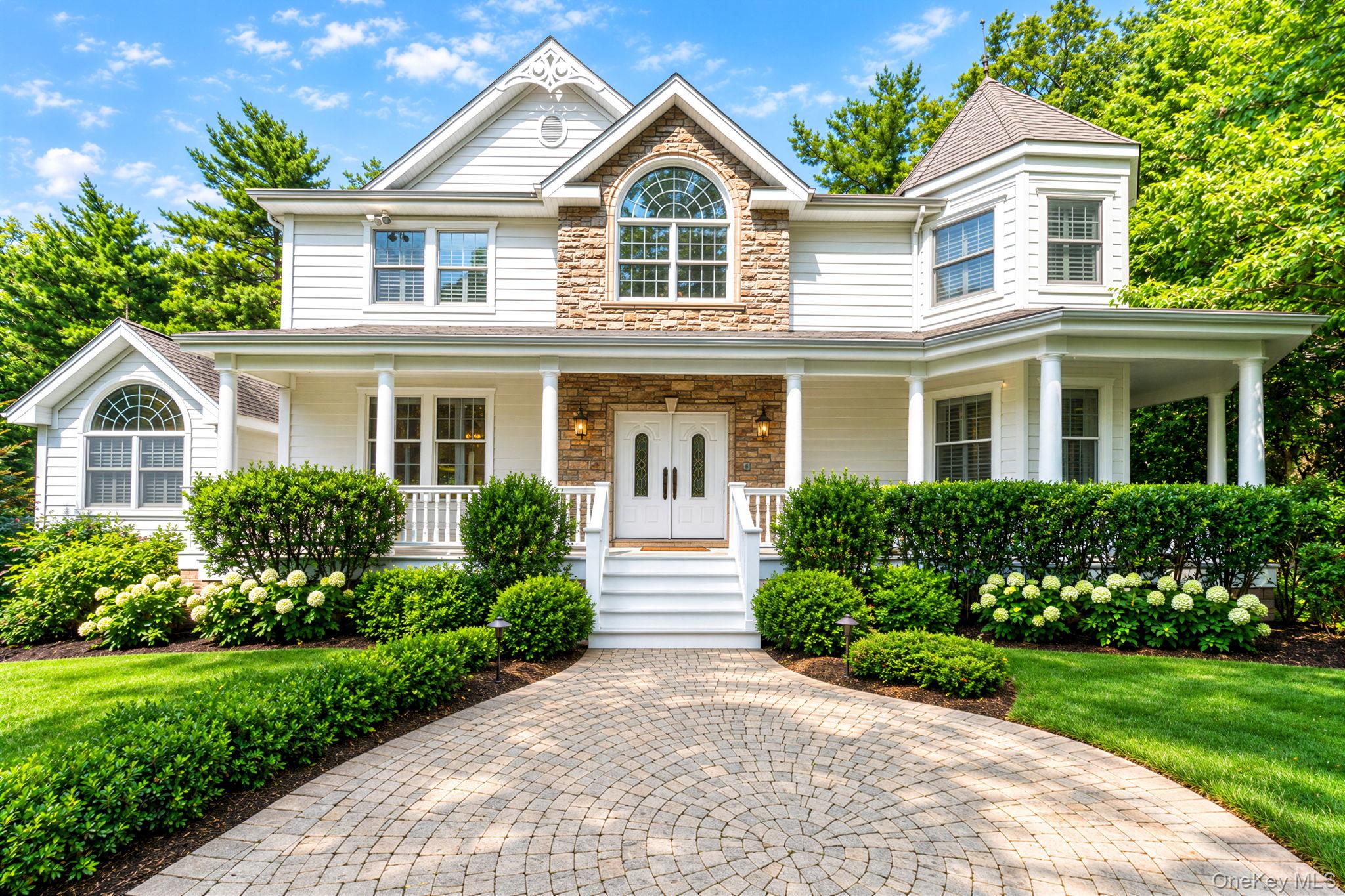Two-story white house with stone accents, a columned porch, and a curved paver driveway.