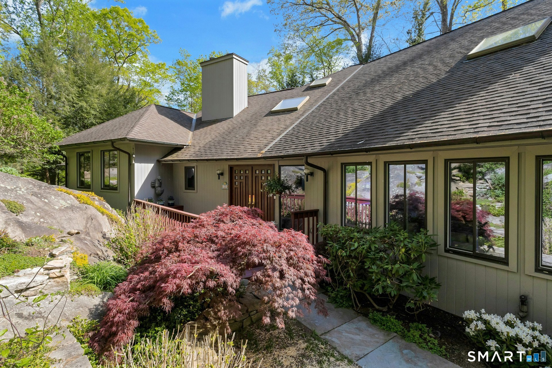 Home exterior with roof skylights, stone landscaping, and a red-leaved Japanese maple.