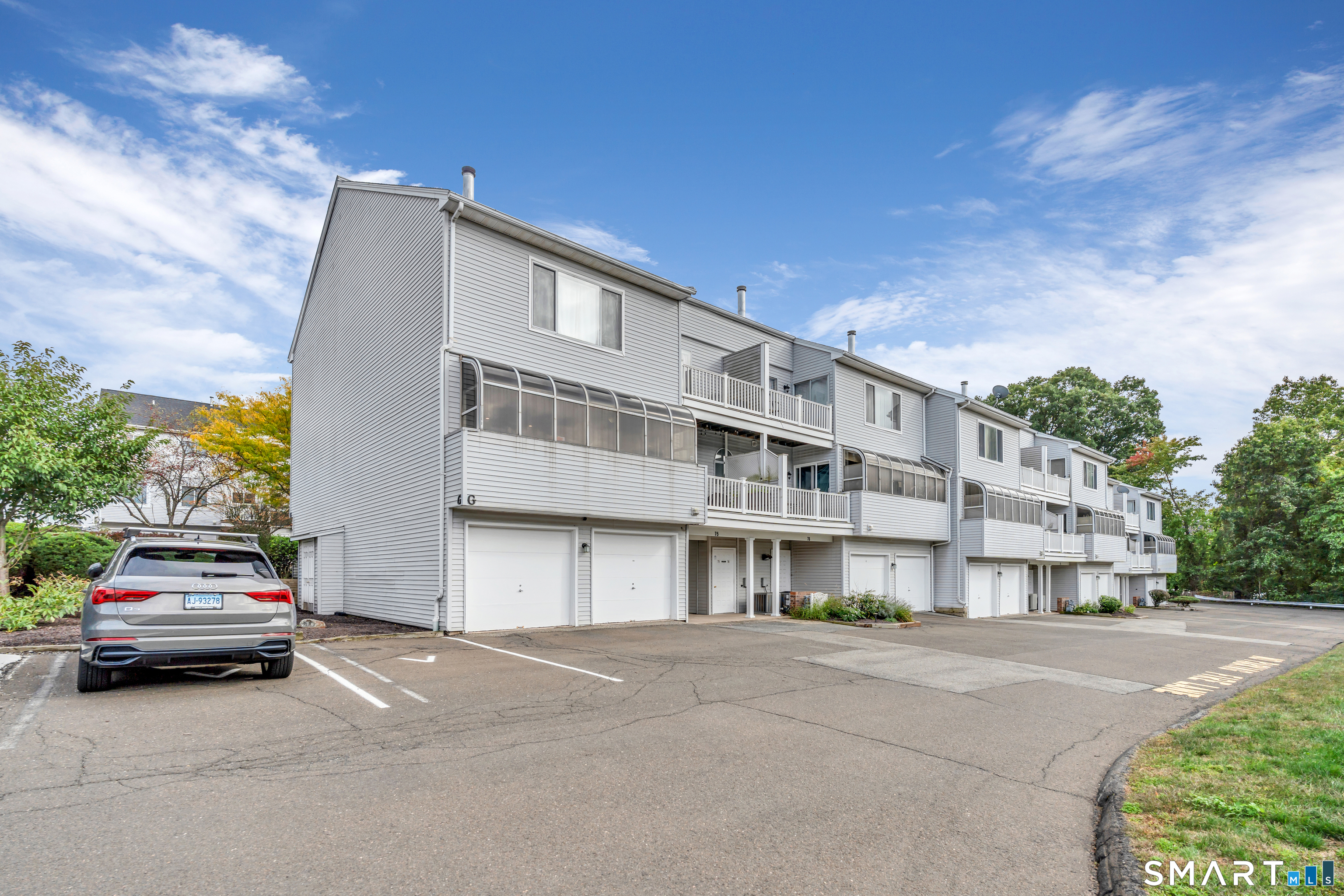 Row of light-gray homes with balconies and garages beside a parking area.