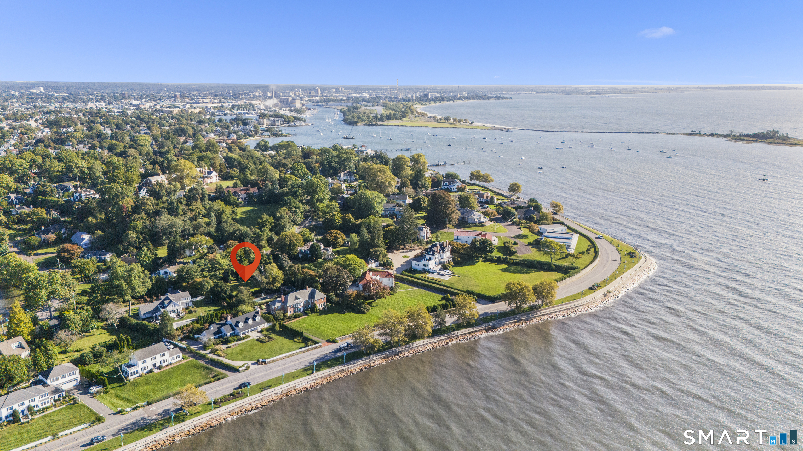 Aerial coastal neighborhood with a red location pin, waterfront homes, and sailboats across the bay.