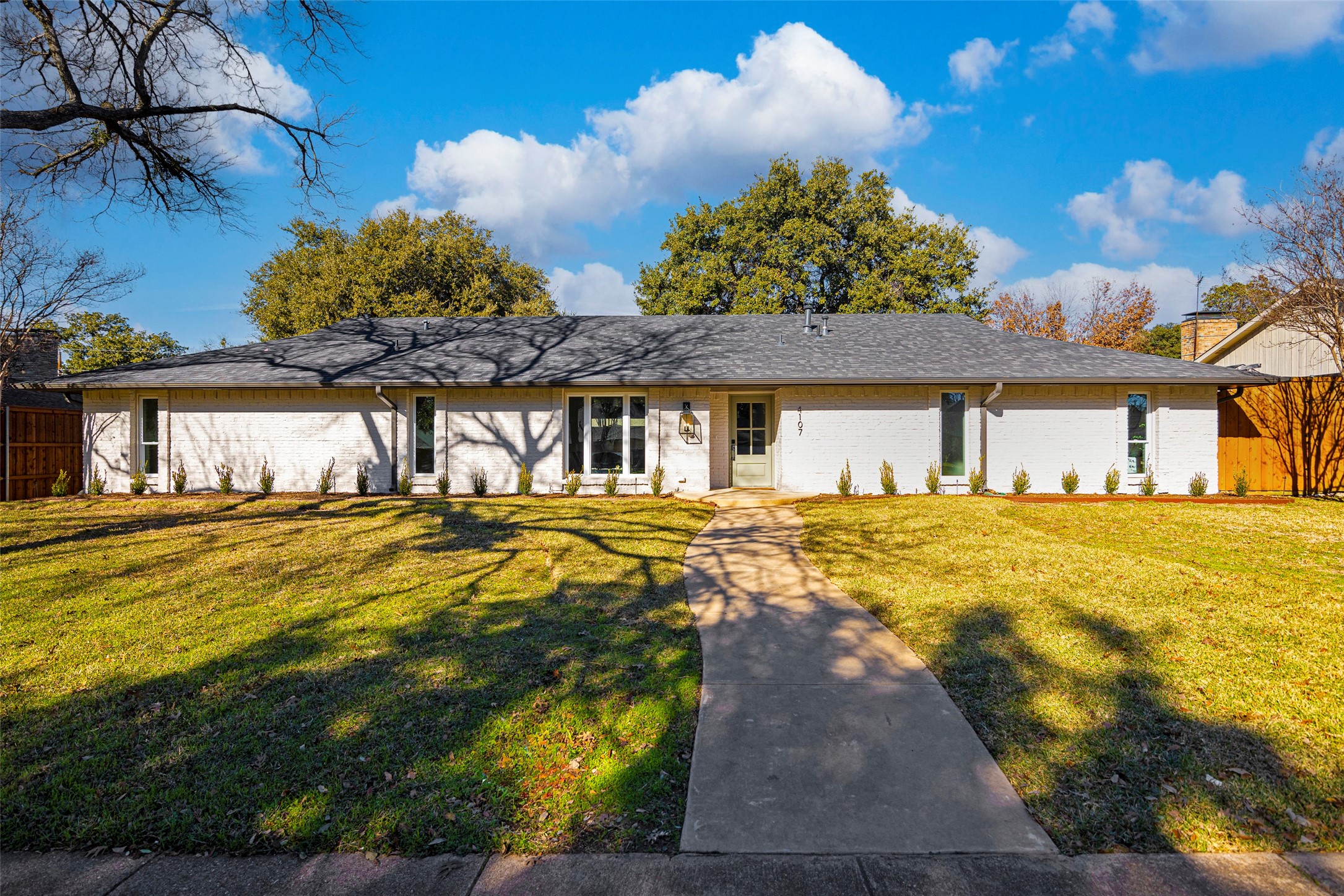 Single-story white brick home with a dark shingle roof and curved walkway across a broad lawn.