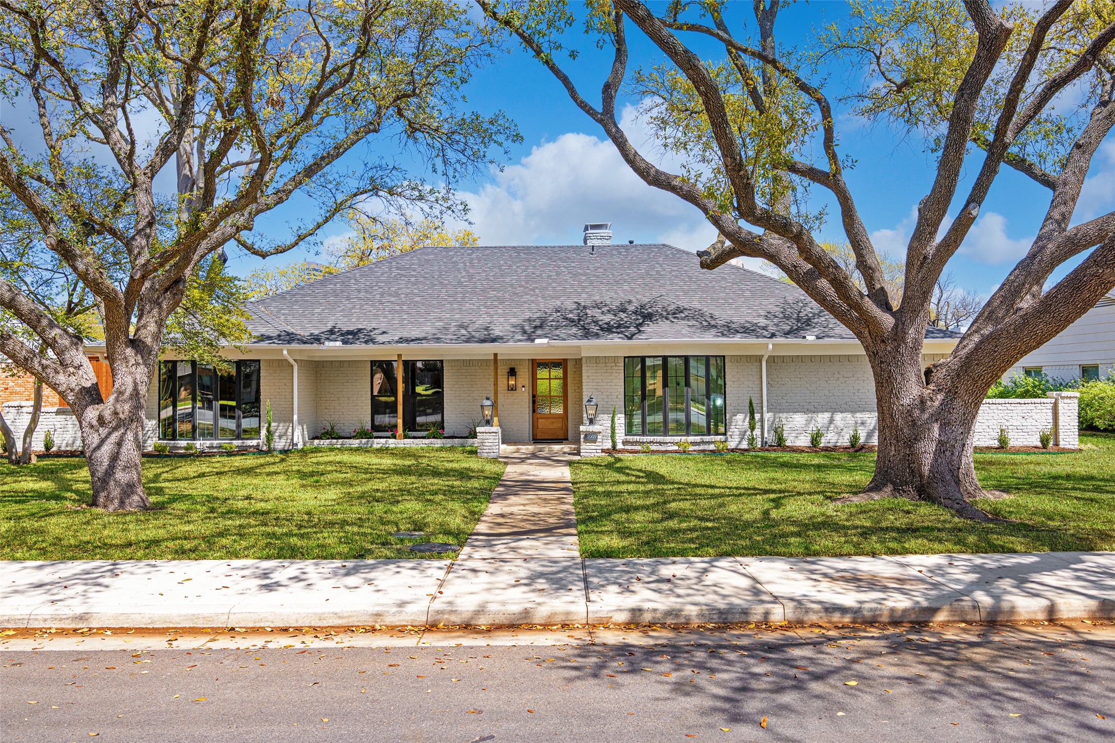 Single-story brick home framed by two large trees, with a central entrance and walkway across the lawn.