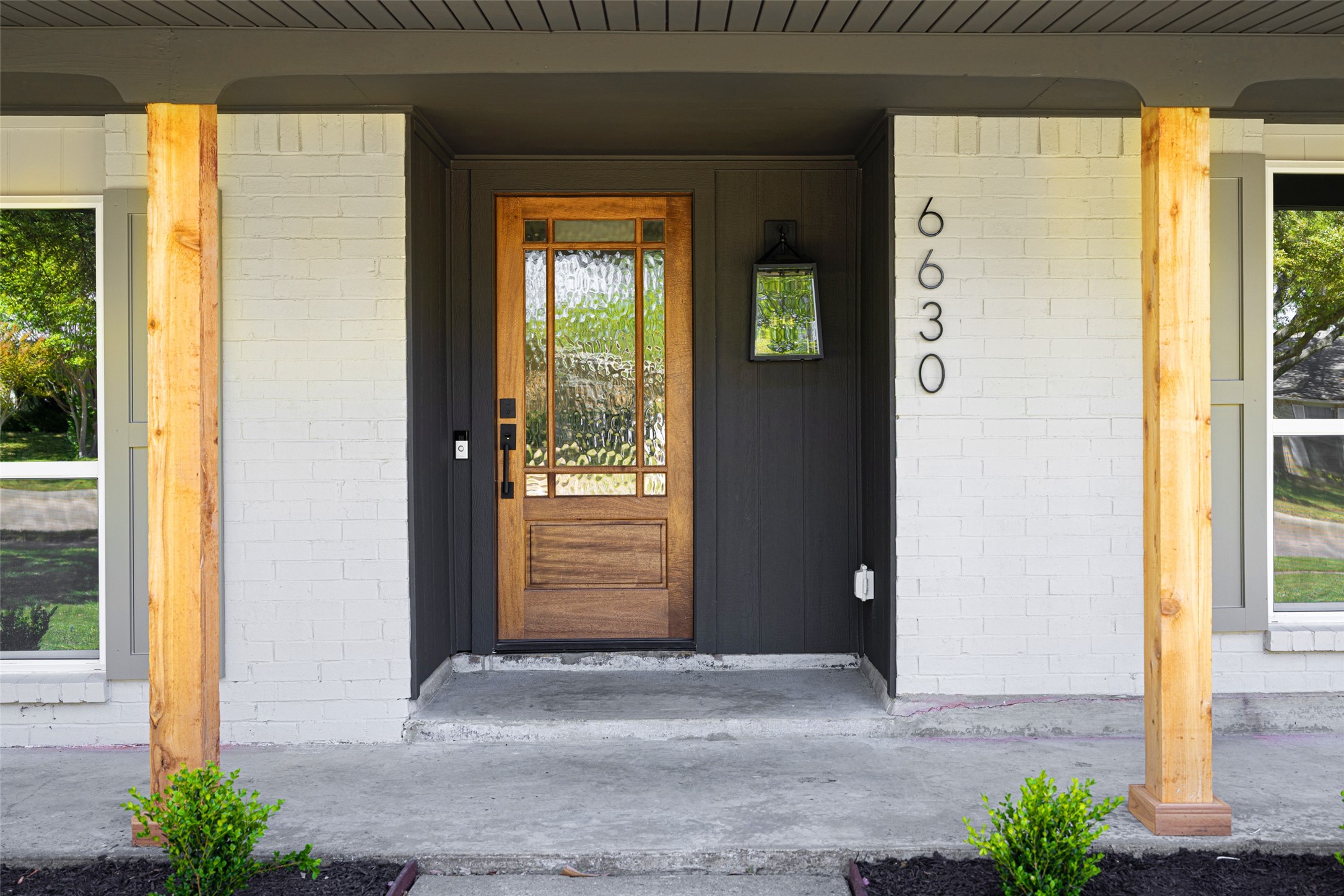 Front entrance with a wood-and-glass door, dark recessed entry, white brick, and timber porch posts.