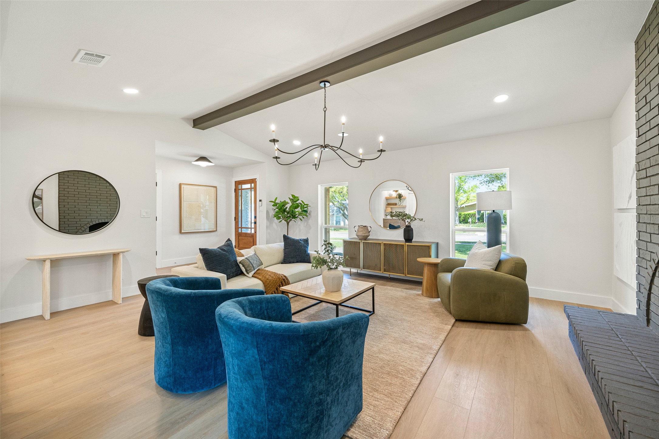 Staged living room with blue velvet chairs, a cream sofa, and a brick fireplace.