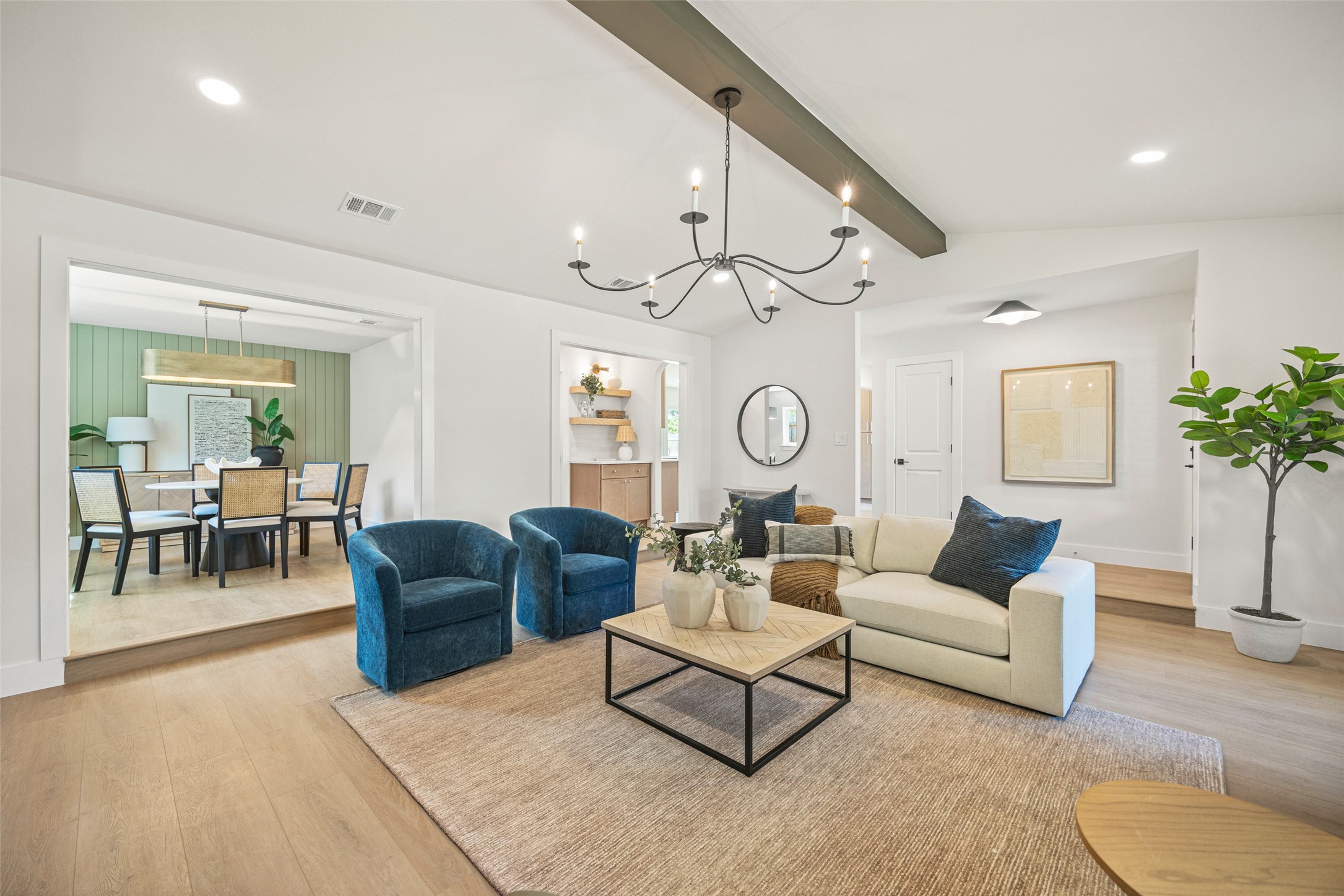 Staged living room with blue armchairs, cream sofa, and adjoining dining area with a sage green paneled wall.