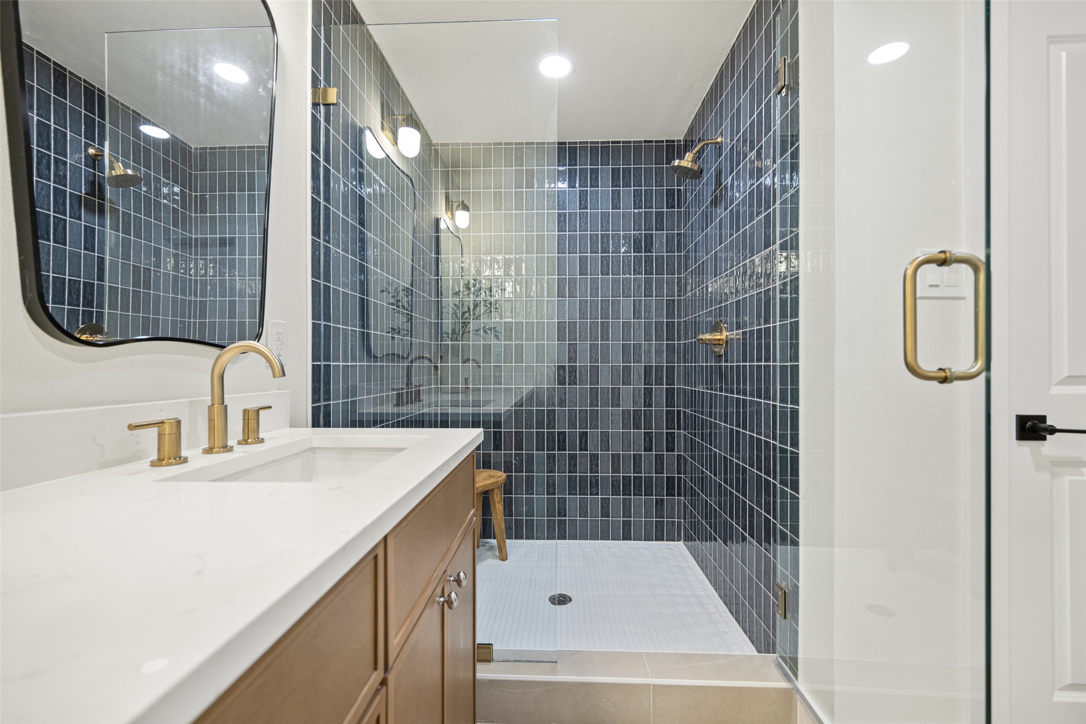 Bathroom vanity with gold fixtures beside a glass-enclosed shower with dark blue-gray tile.