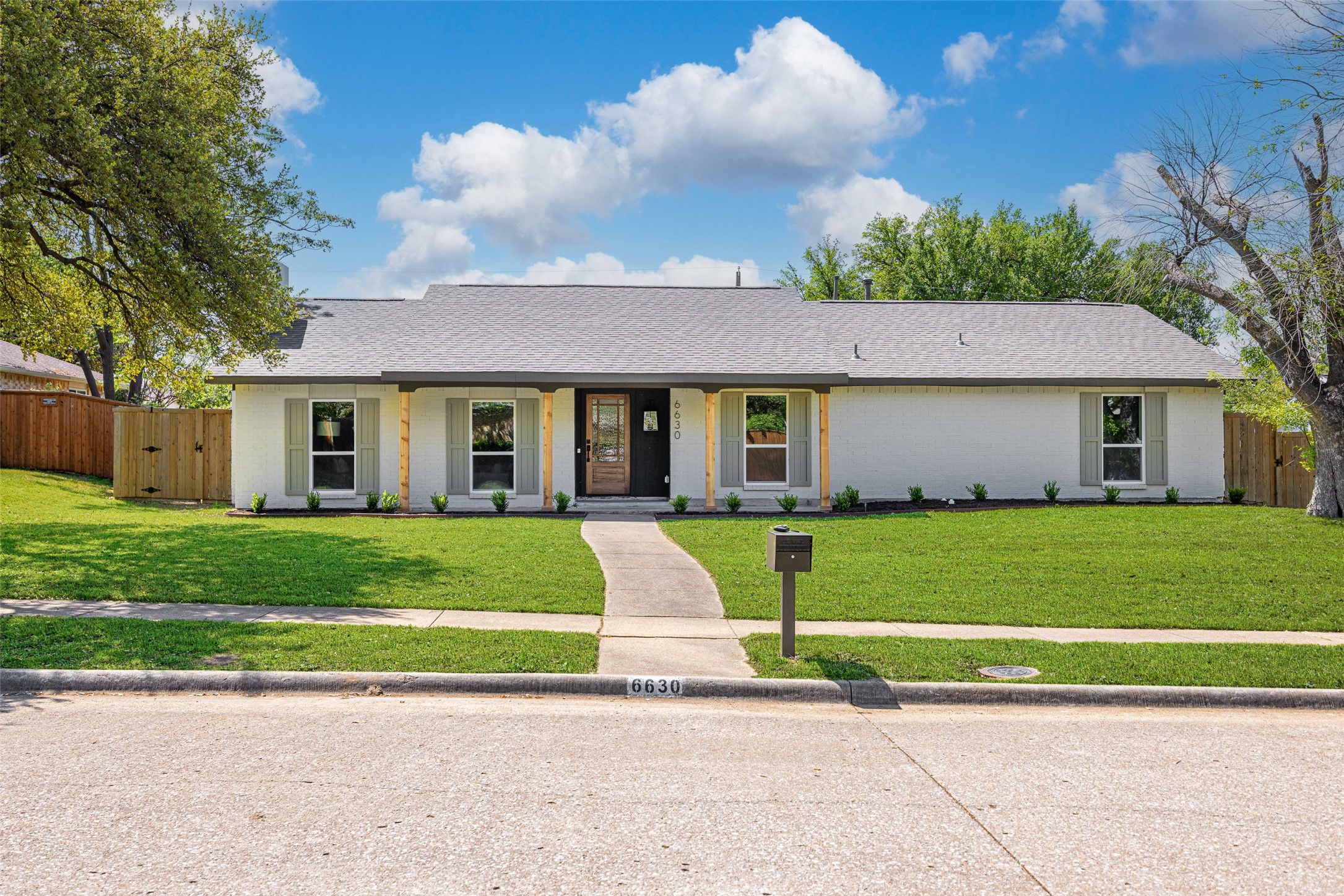 Single-story white brick house with green shutters, a covered entry, and a curved front walkway.
