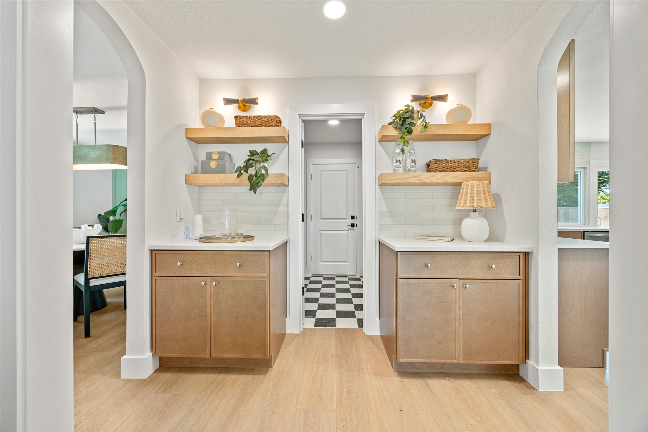 Hallway with matching light wood built-in cabinets, floating shelves, and a checkered floor through the doorway.