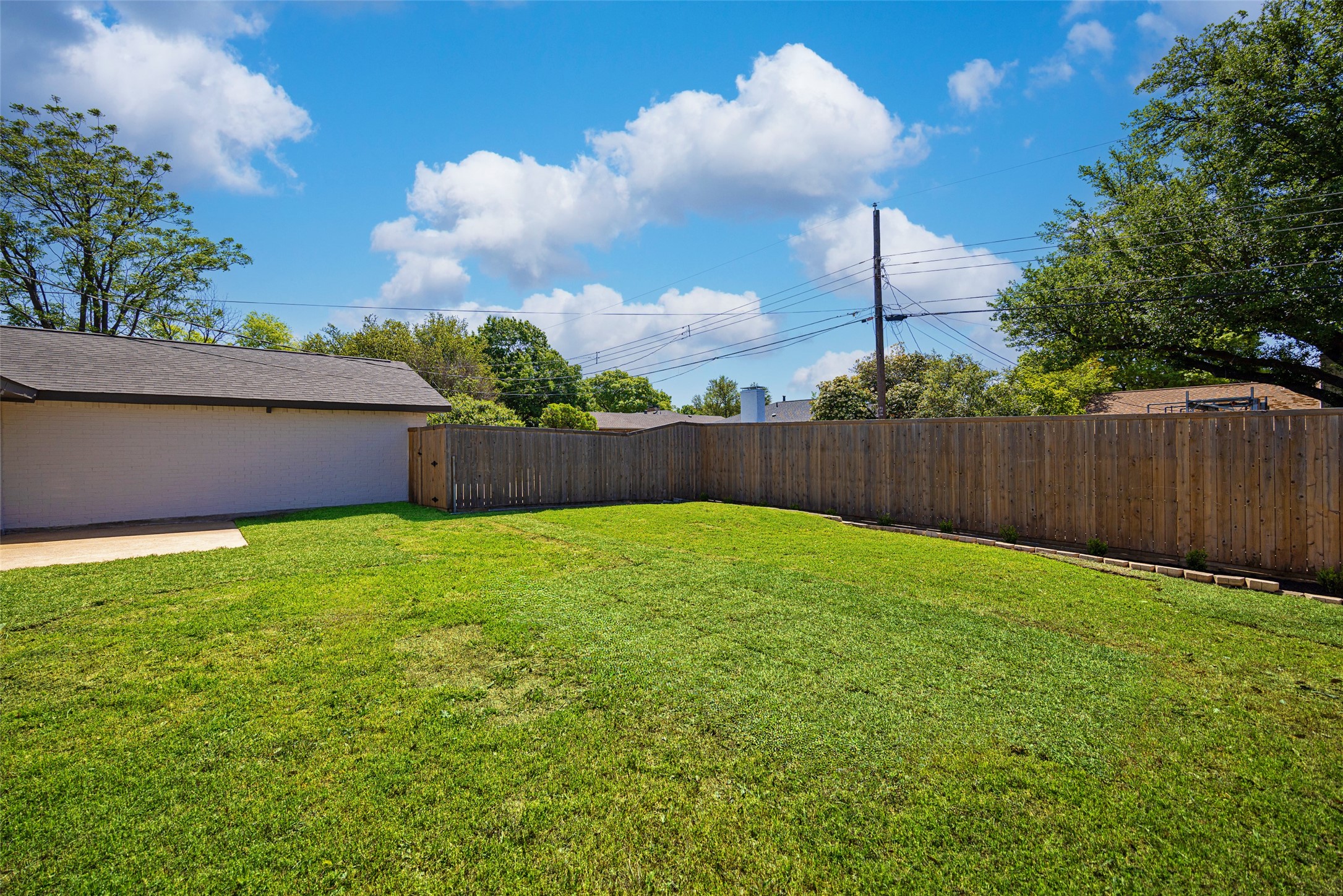 Spacious grassy backyard enclosed by a wooden privacy fence, with a brick outbuilding along one side.