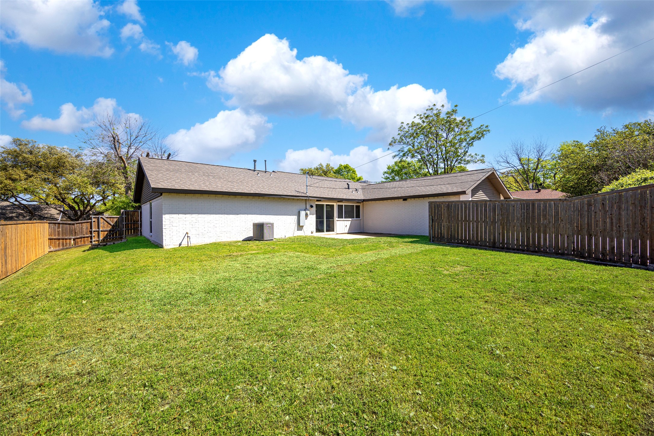 House rear and broad fenced lawn with mature trees.