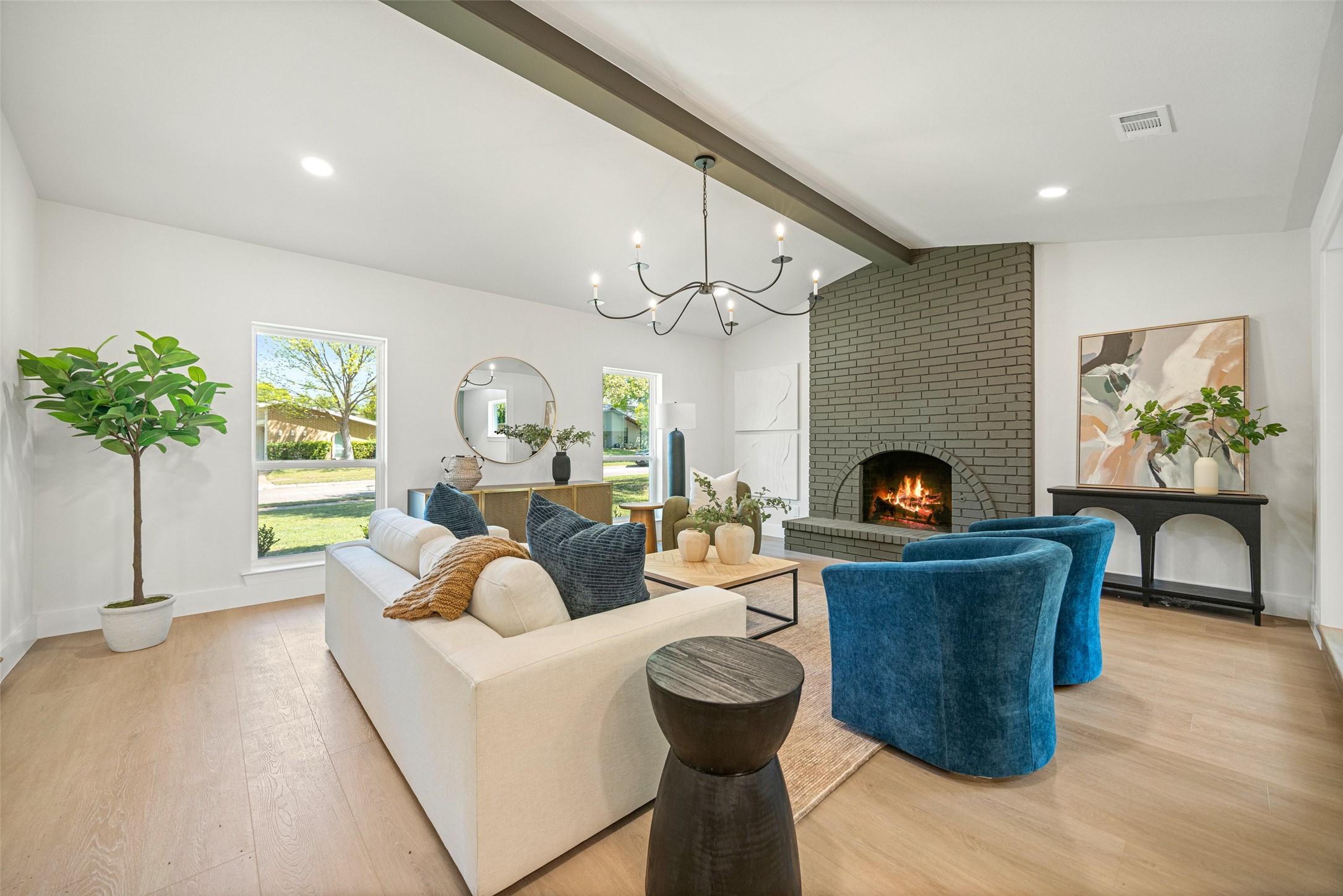 Staged living room with a tall gray brick fireplace, blue armchairs, and vaulted ceiling.