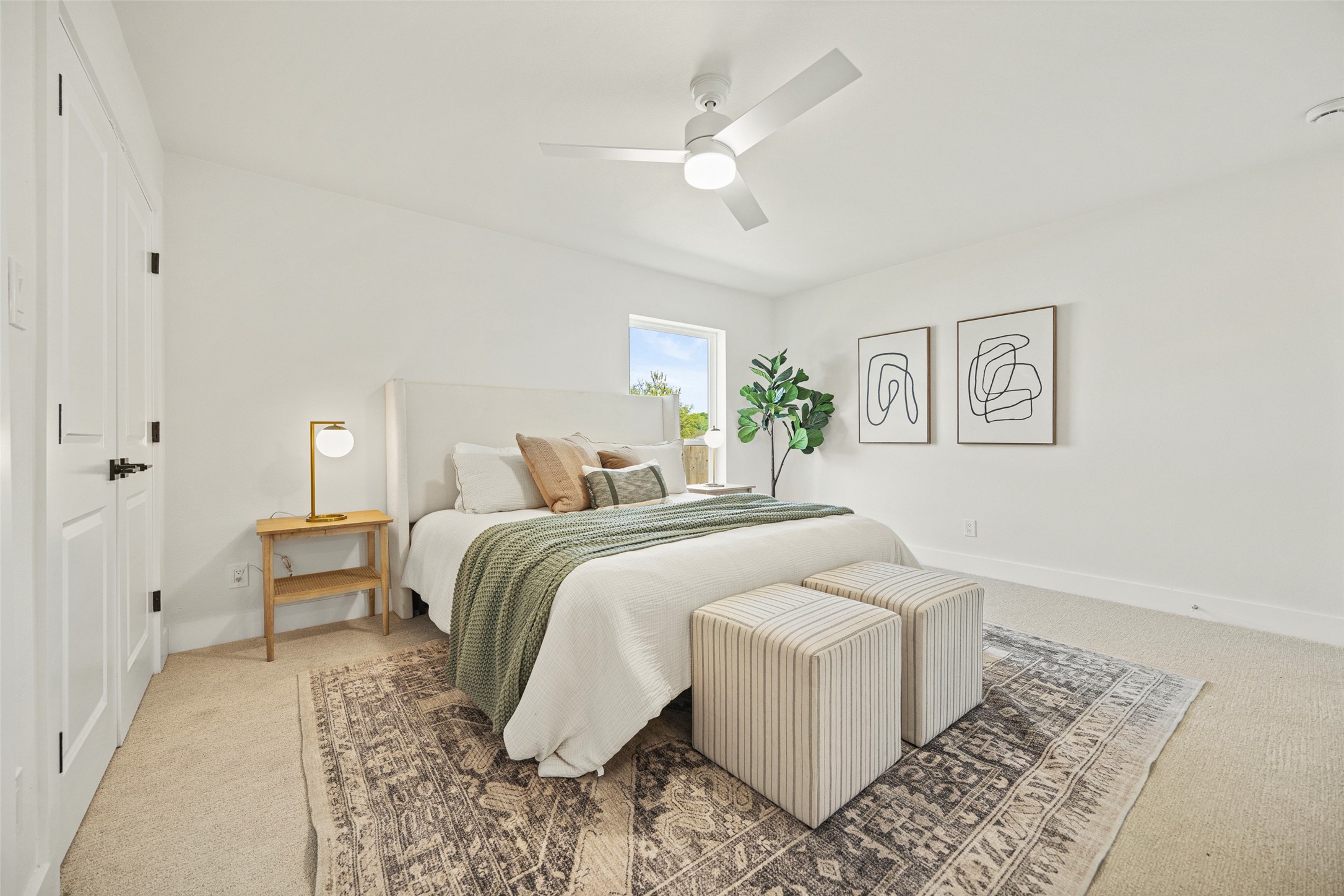 Staged bedroom with a white bed, green throw, striped benches, patterned rug, and ceiling fan.