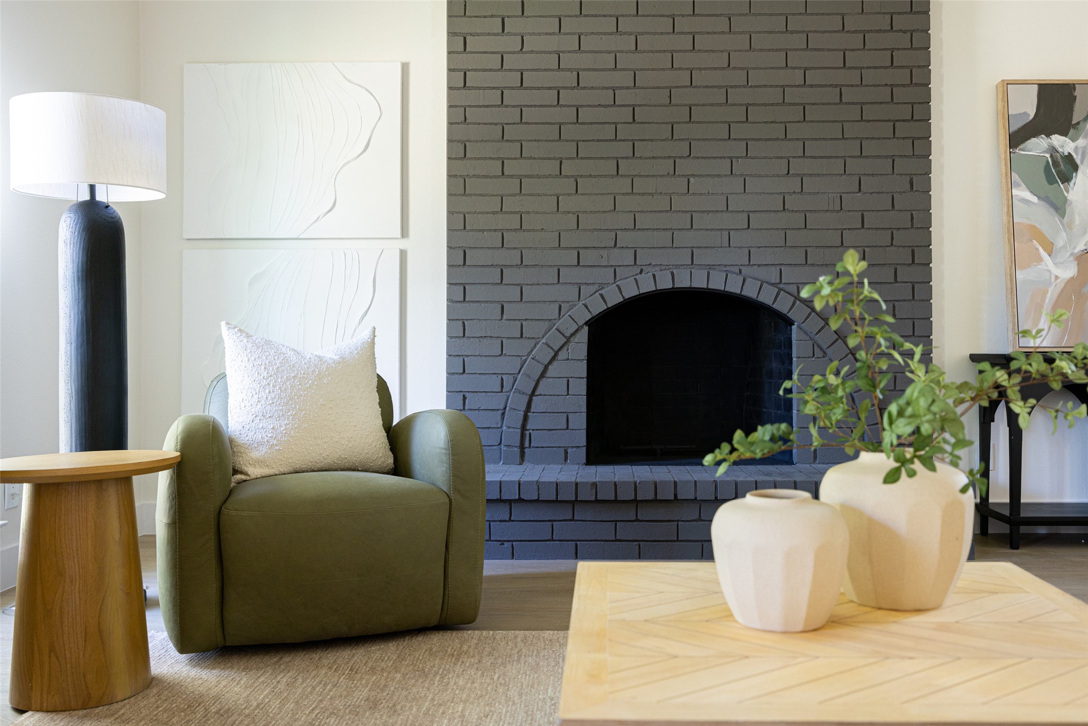 Living room with a dark gray brick fireplace, olive-green armchair, and light wood coffee table.