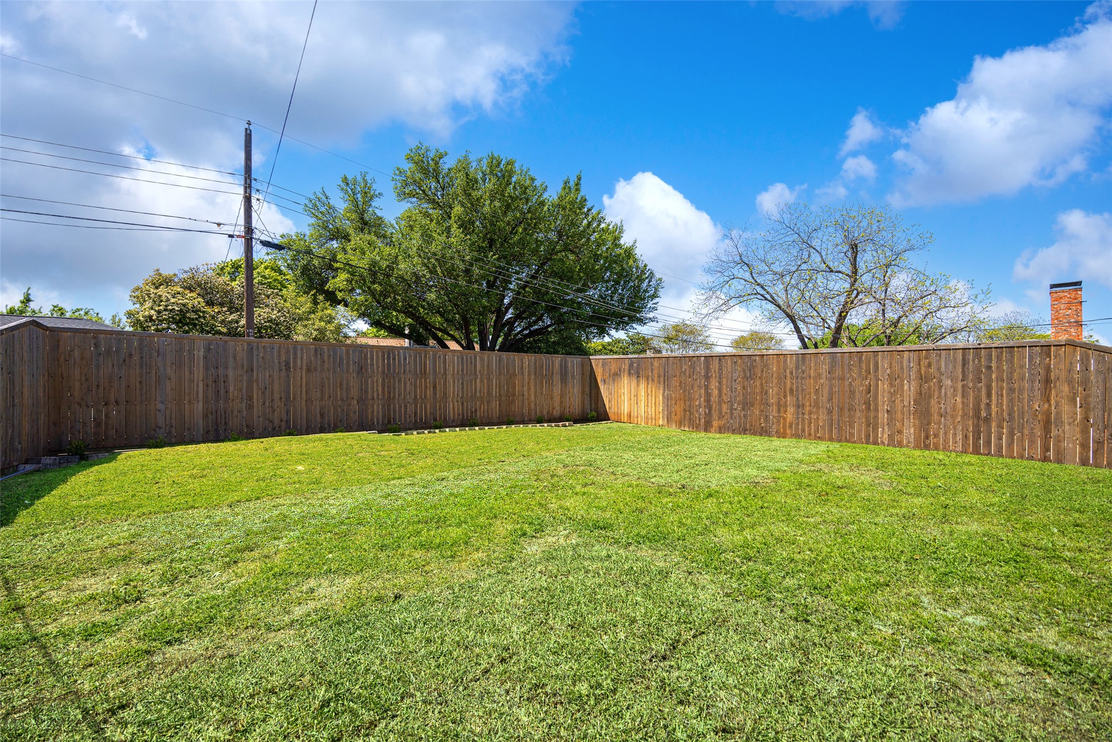Fenced backyard with a wide green lawn and tall wooden privacy fence.