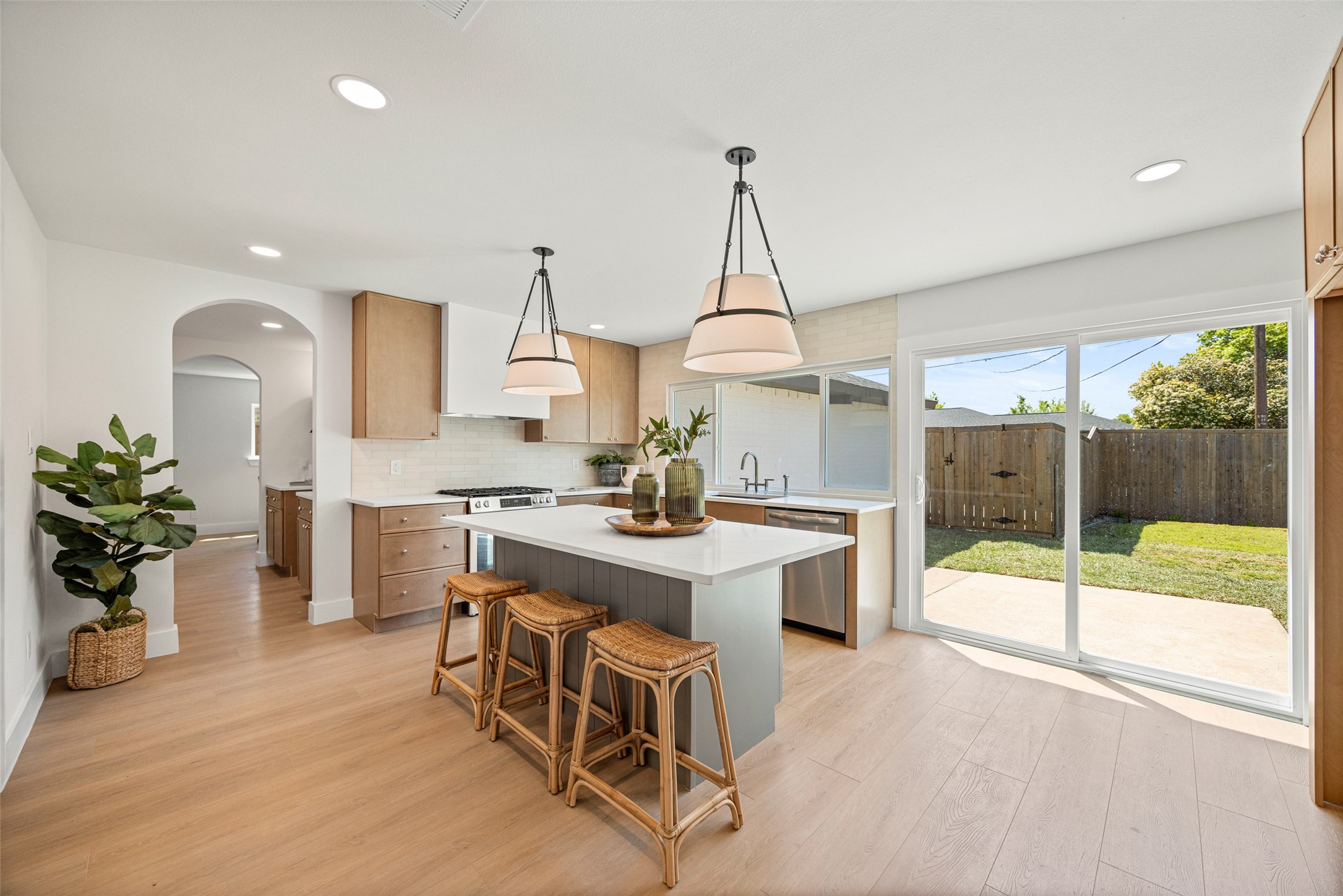 Bright kitchen with a large island, woven stools, and sliding doors to a fenced yard.