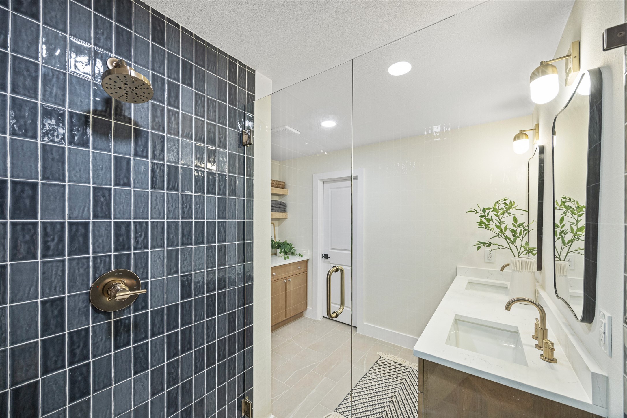Modern bathroom with dark blue tiled shower, glass enclosure, and double vanity with brass fixtures.
