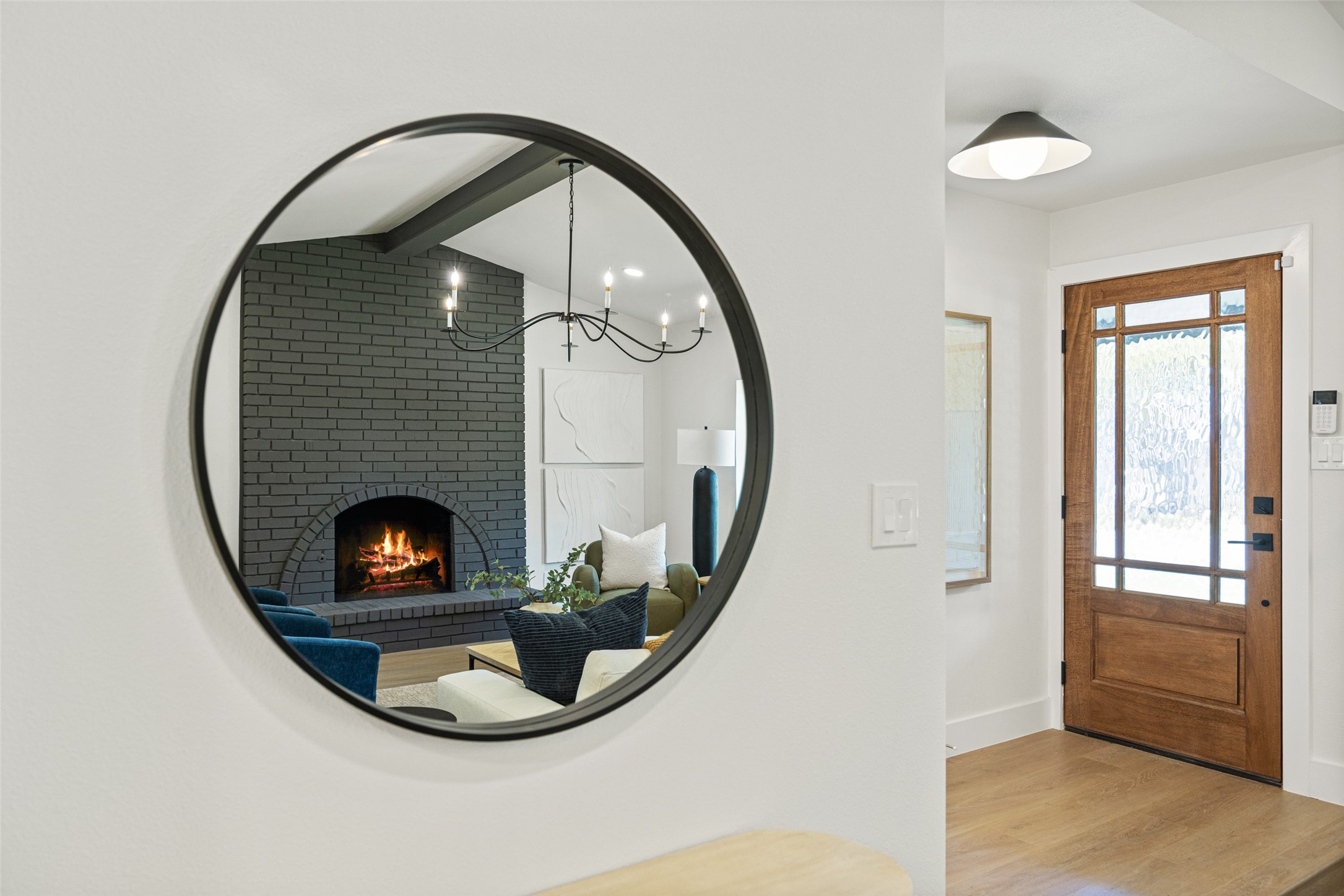 Home entryway with a wood-and-glass front door and round mirror reflecting a living room fireplace.