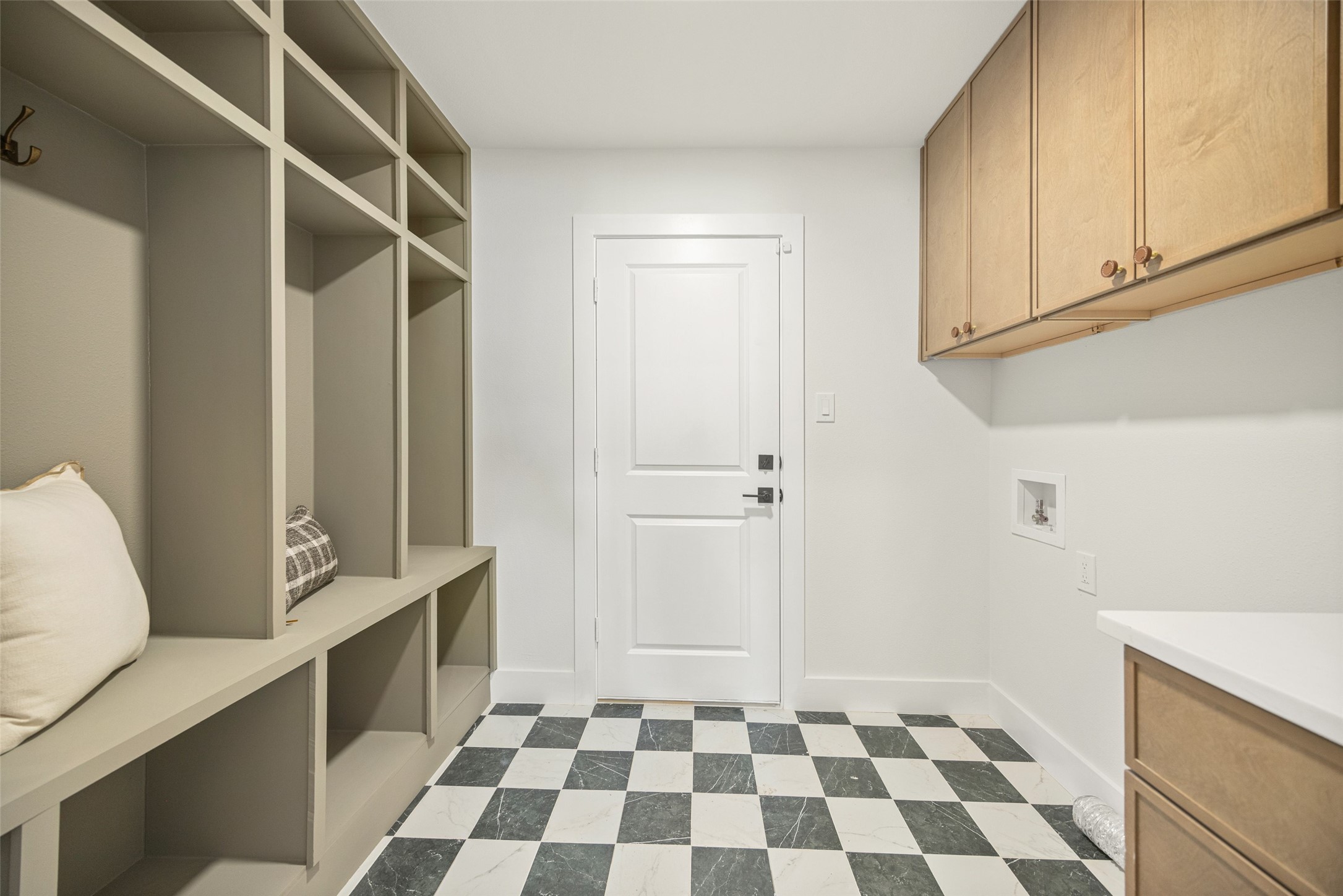Utility room with built-in cubbies, washer hookups, light wood cabinets, and checkerboard tile flooring.