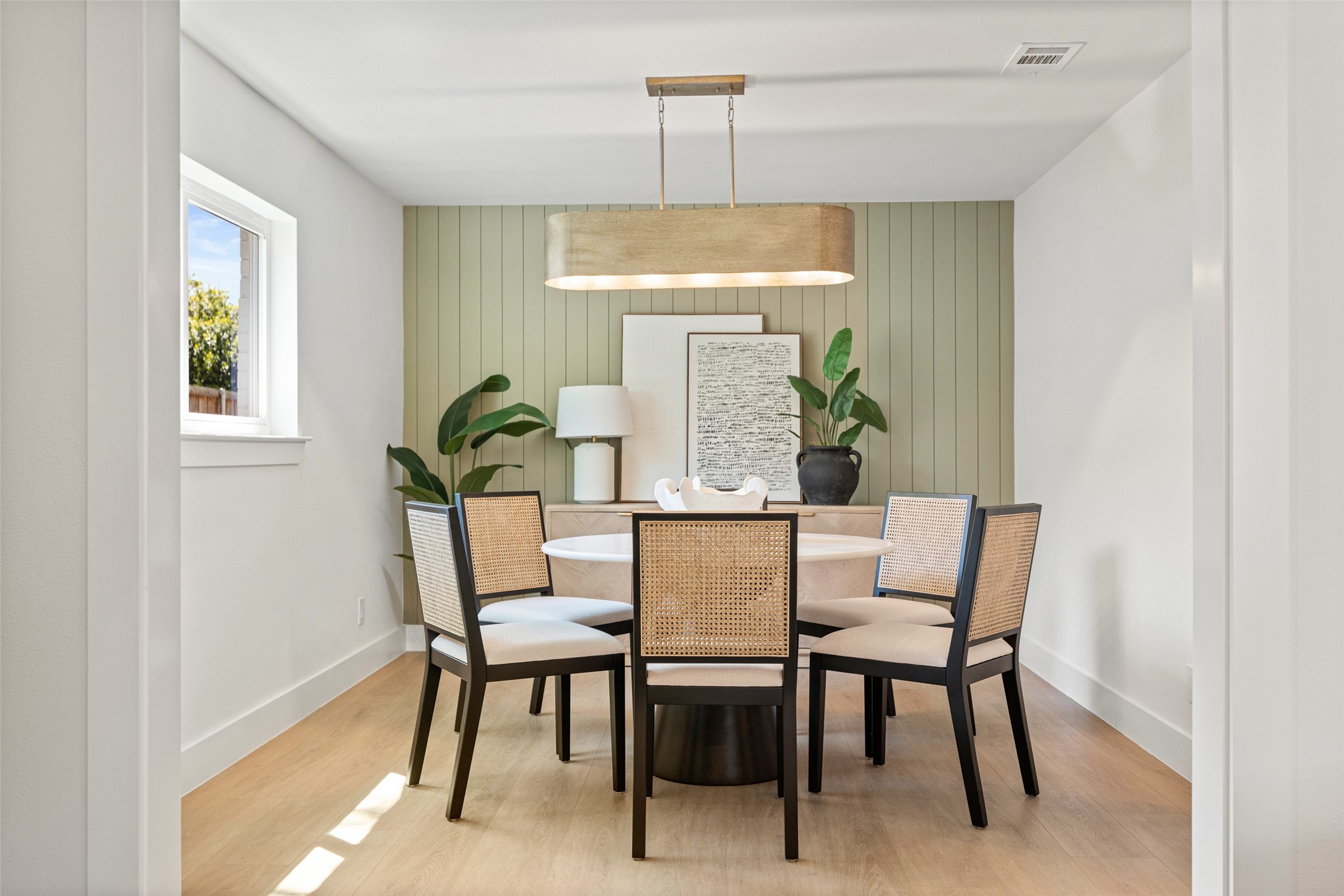 Dining room with a round table, woven chairs, and sage green paneled wall.