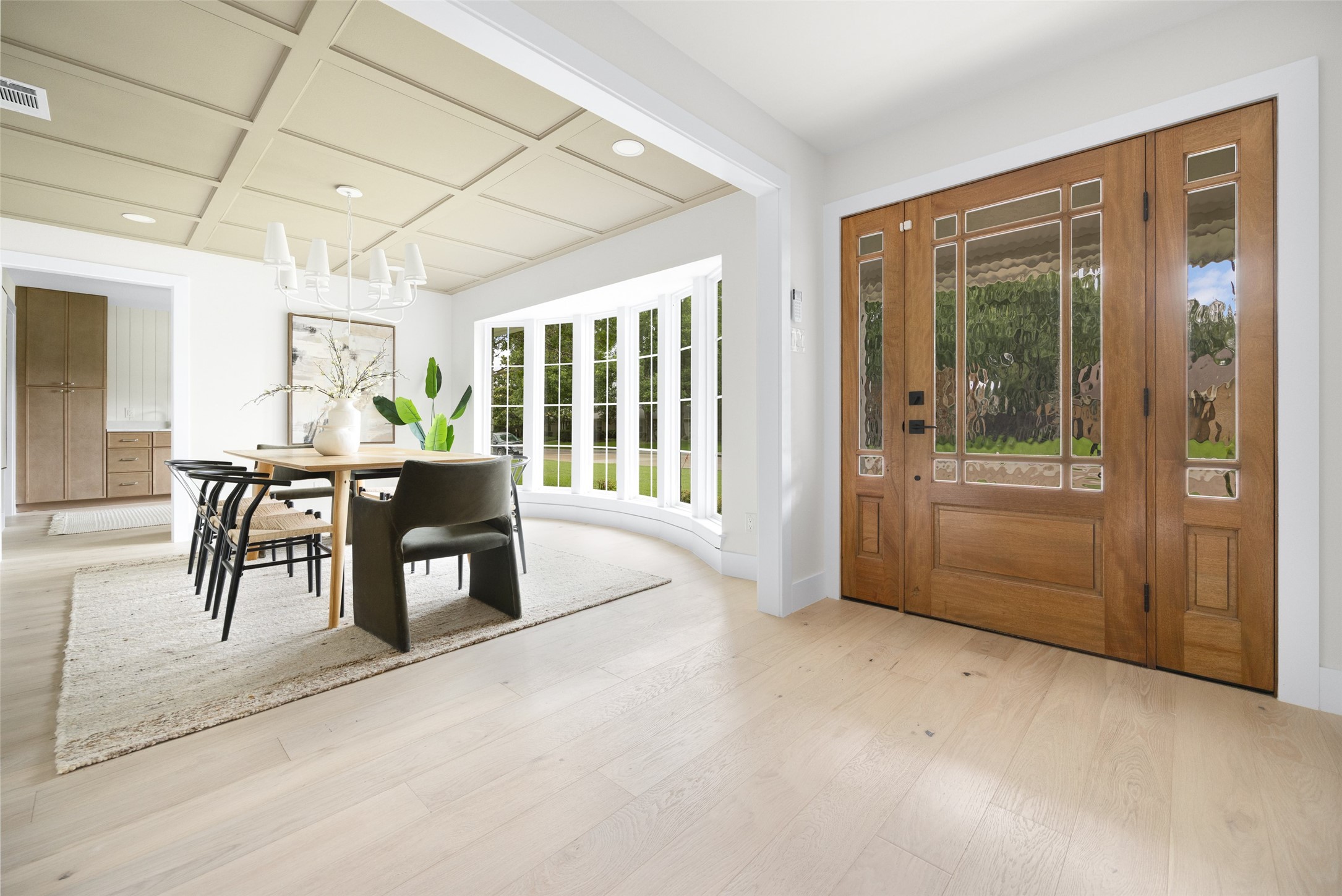 Dining room with a coffered ceiling, curved windows, and a wood front door with decorative glass.