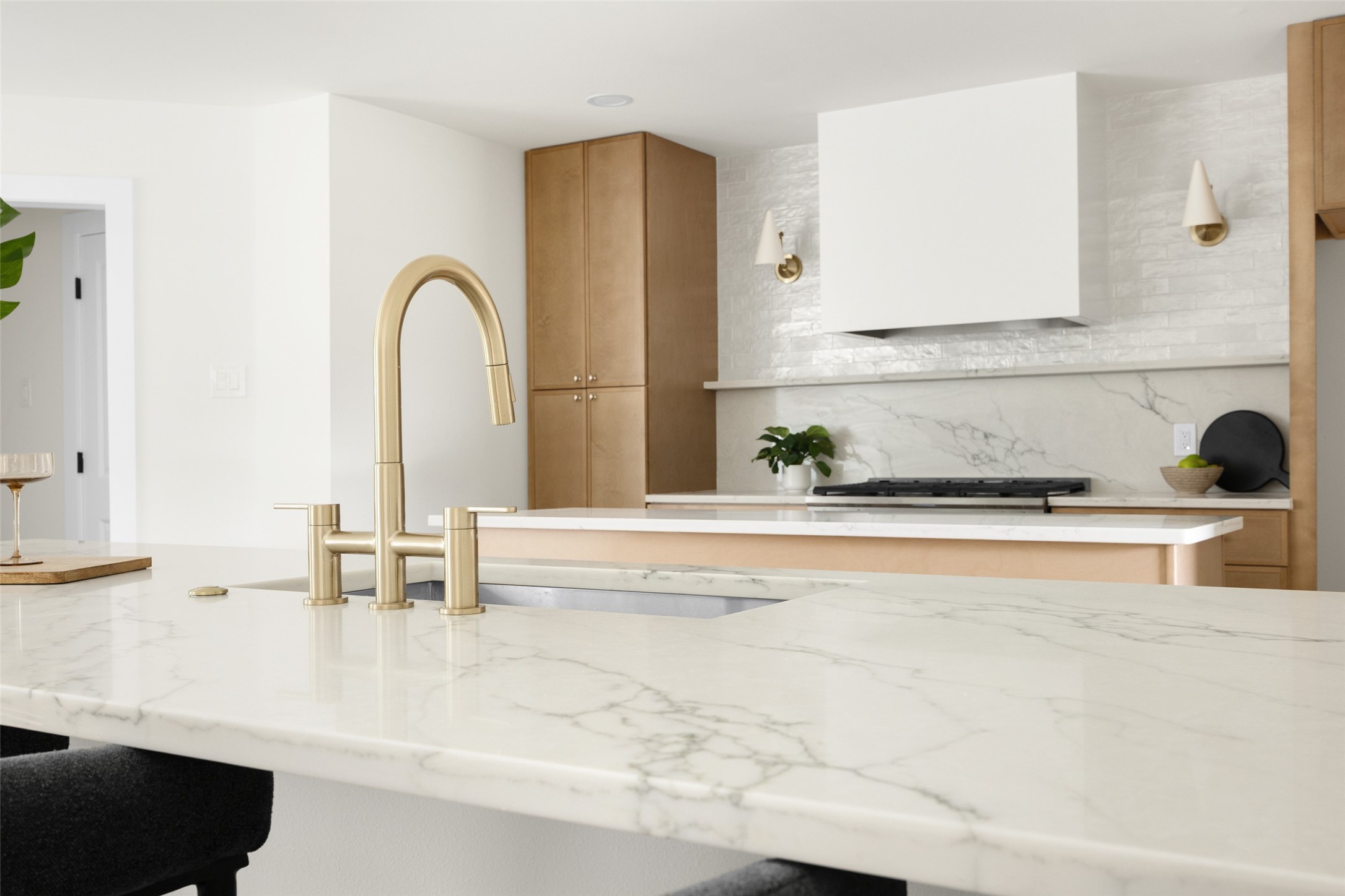 Modern kitchen with a marble island, tall gold faucet, light wood cabinetry, and gas cooktop.