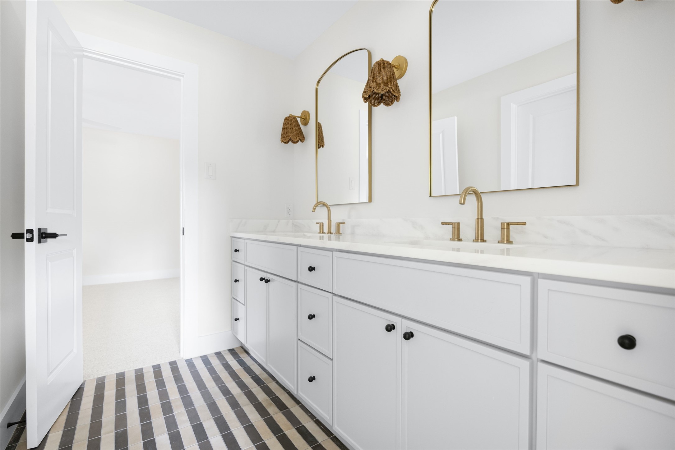 Bright bathroom with a white double vanity, brass fixtures, arched mirrors, and patterned tile floor.
