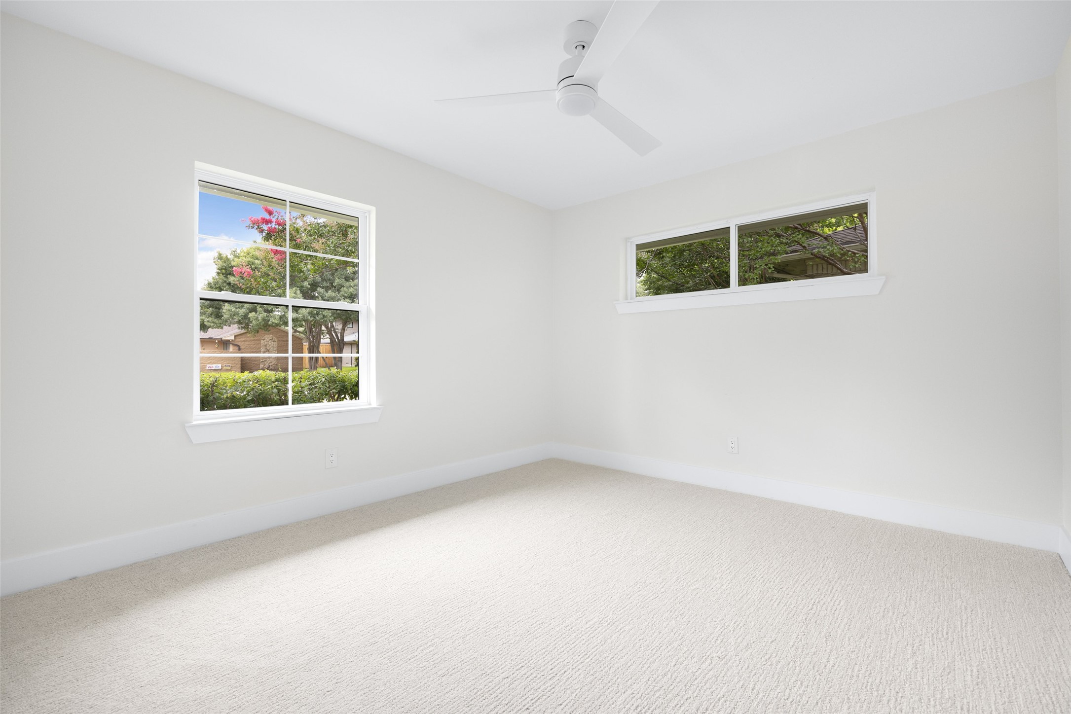 Empty carpeted room with two windows and a white ceiling fan.