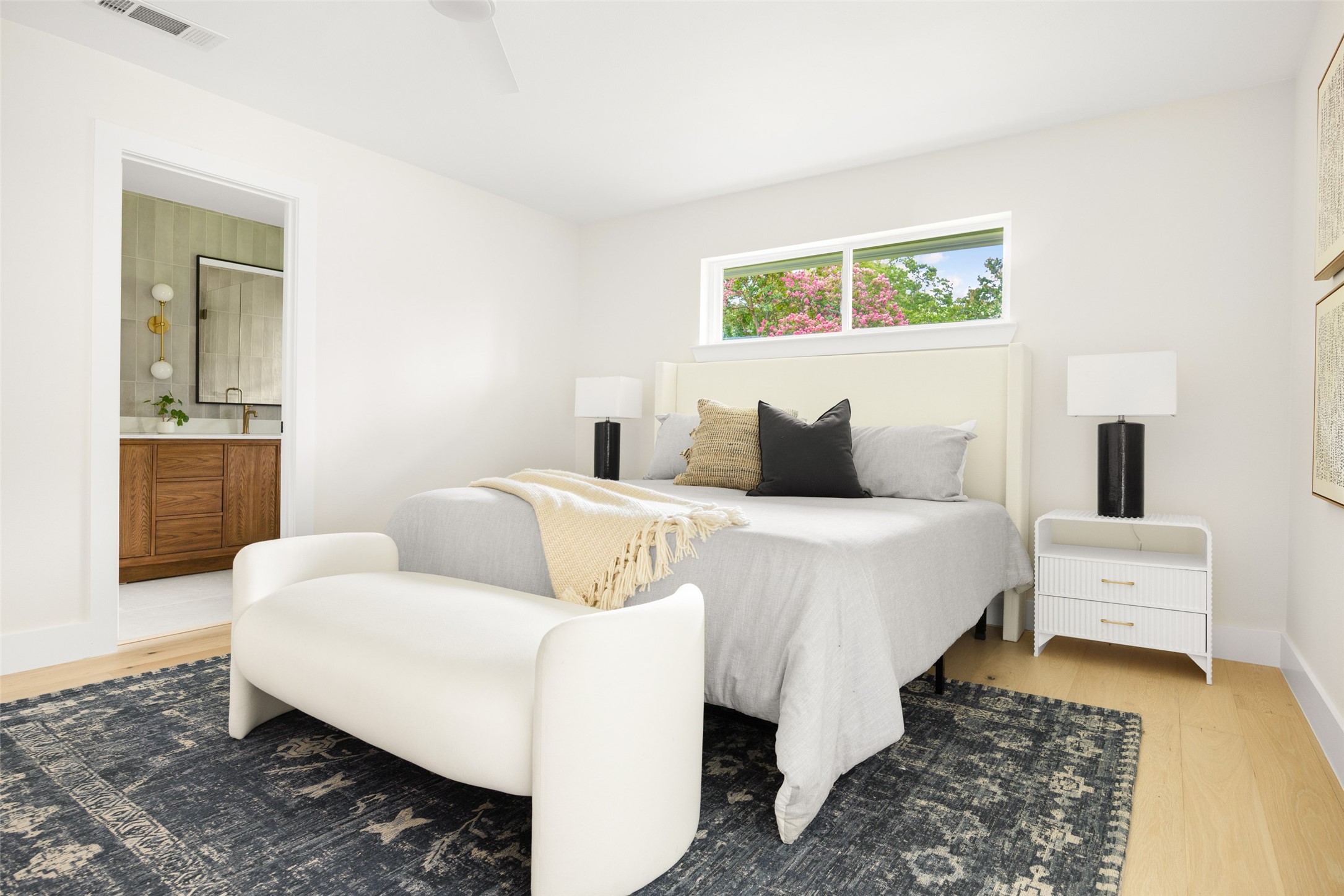 Staged bedroom with a king-size bed, dark patterned rug, and window overlooking flowering trees.