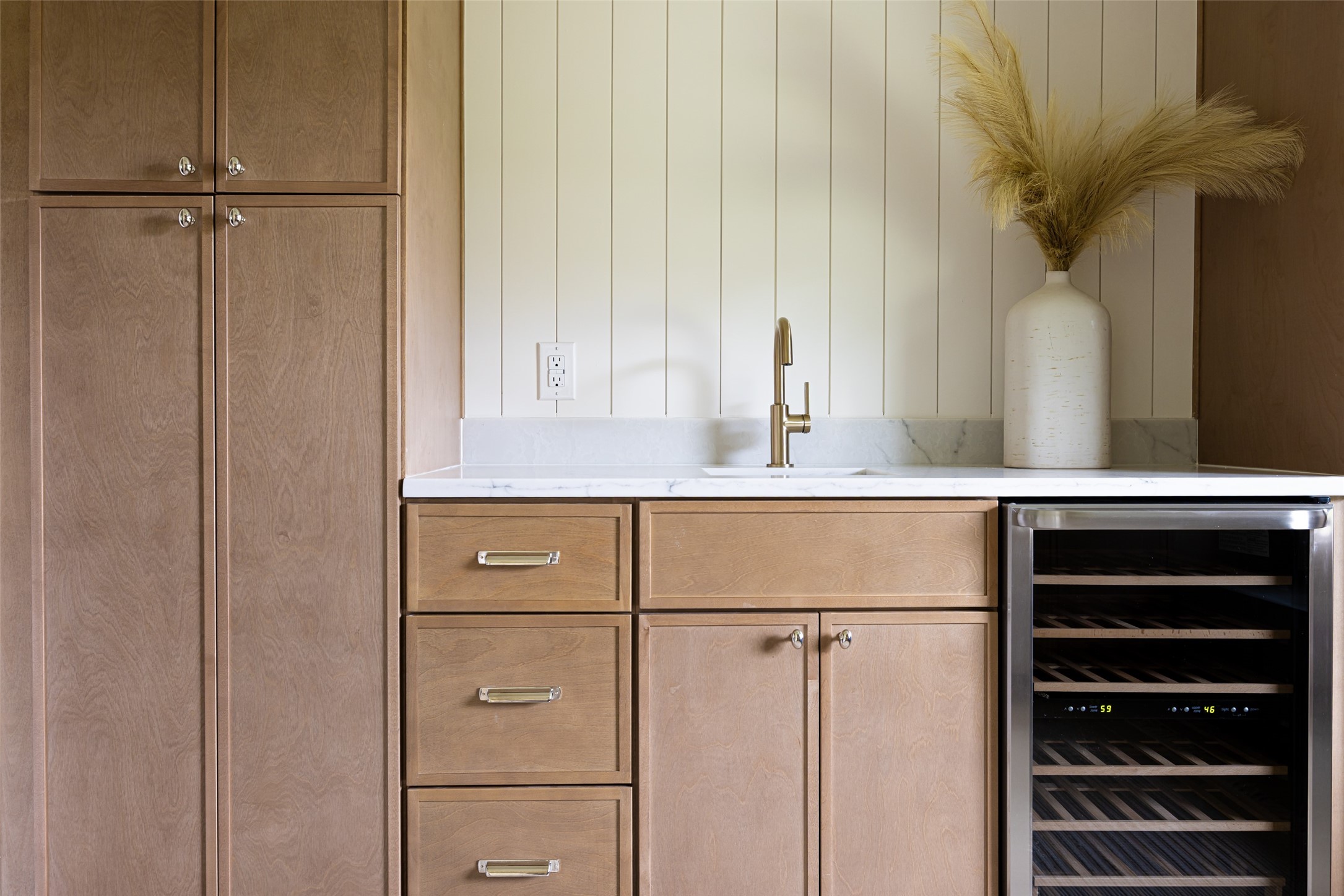 Kitchen with warm wood cabinetry, marble counters, brass faucet, and a built-in wine refrigerator.