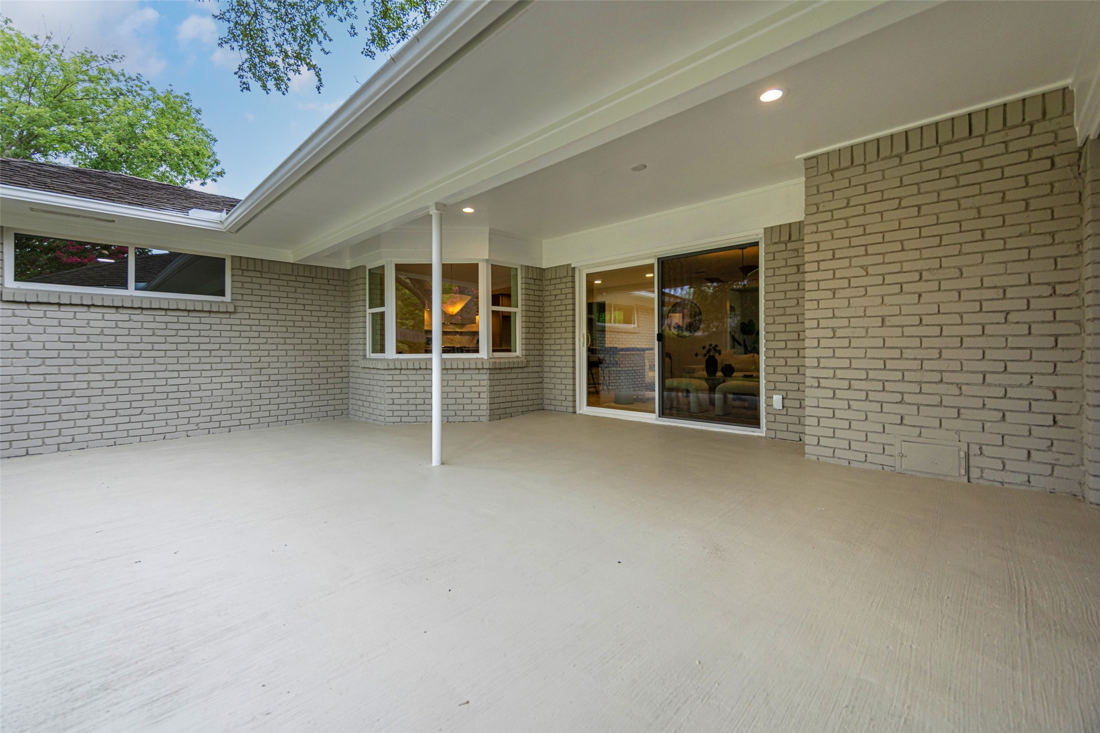 Covered concrete patio with light brick walls and sliding glass doors.