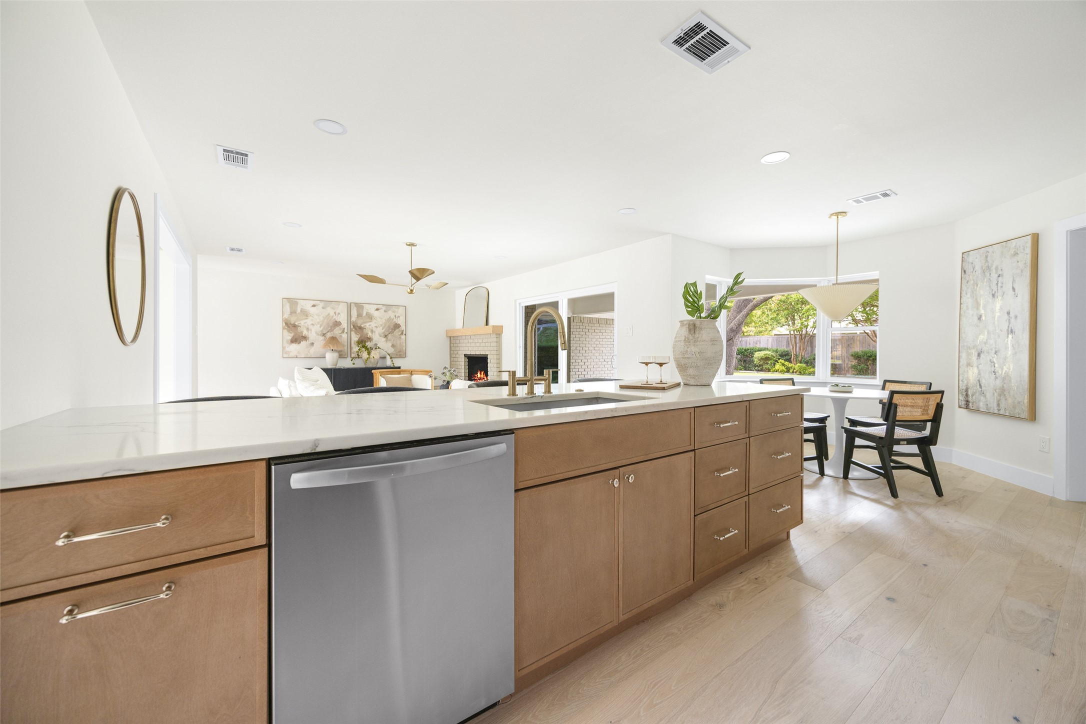 Bright kitchen with a large stone island, wood cabinetry, and an open dining area beside backyard-facing windows.