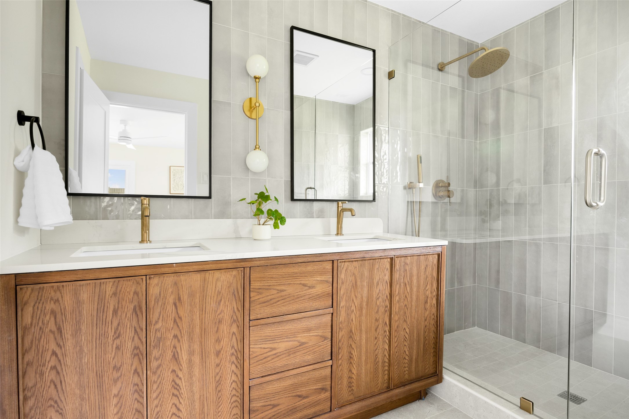Bathroom with a wood double vanity and brass fixtures beside a glass-enclosed tiled shower.