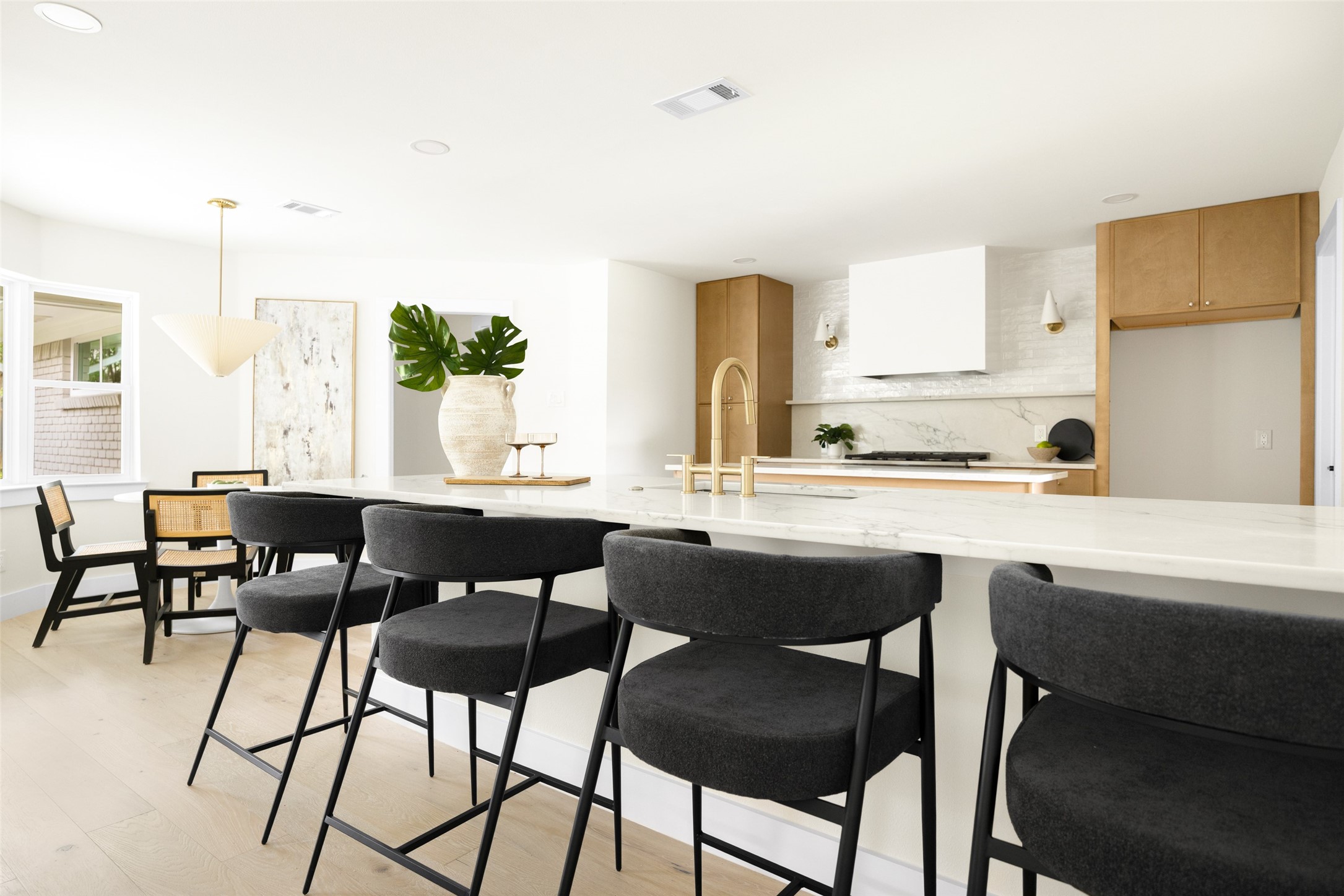 Open-plan kitchen with a marble island, gold faucet, warm wood cabinets, and dark counter stools.