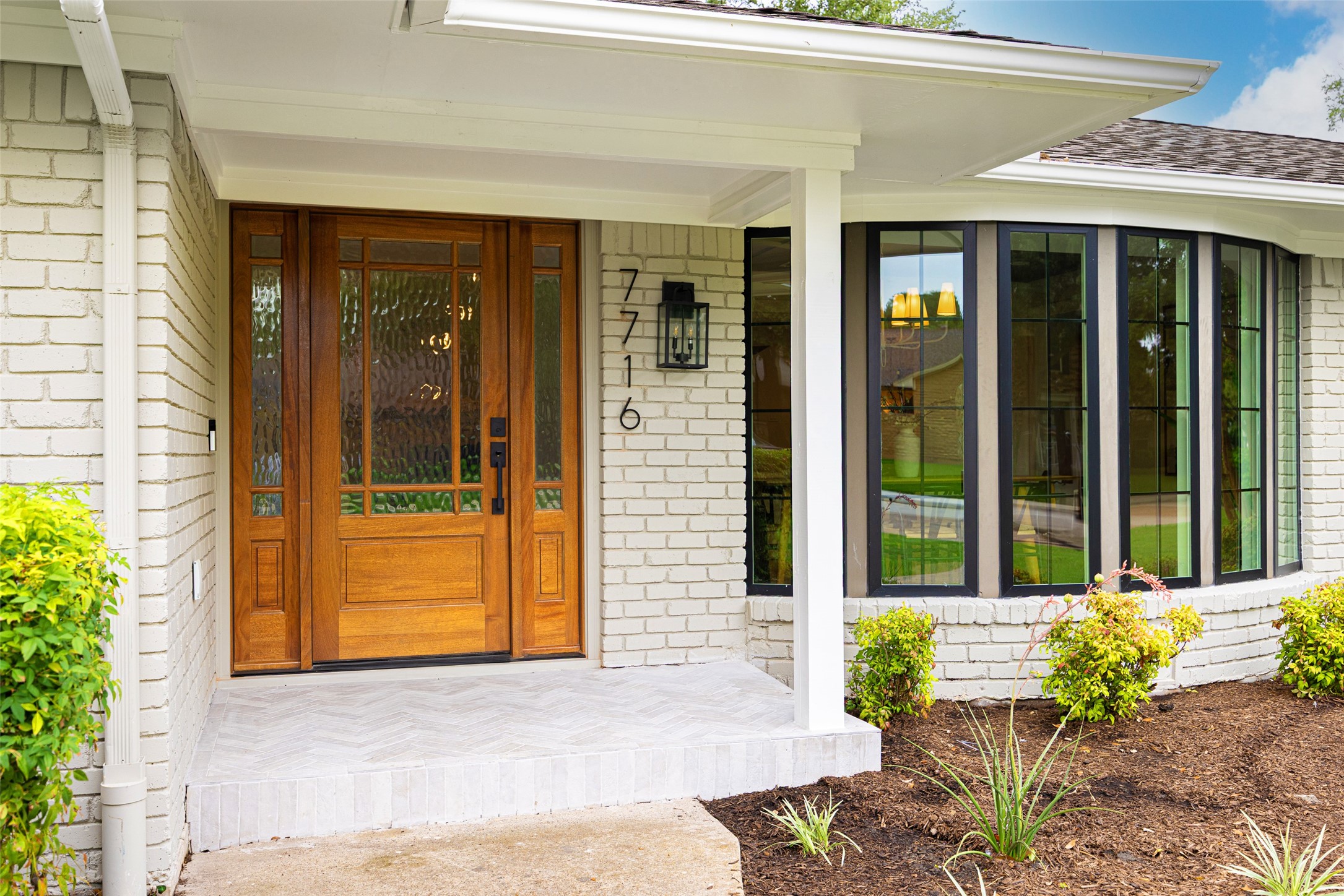 Home entrance with a wood-and-glass door, white brick facade, and black-framed windows.