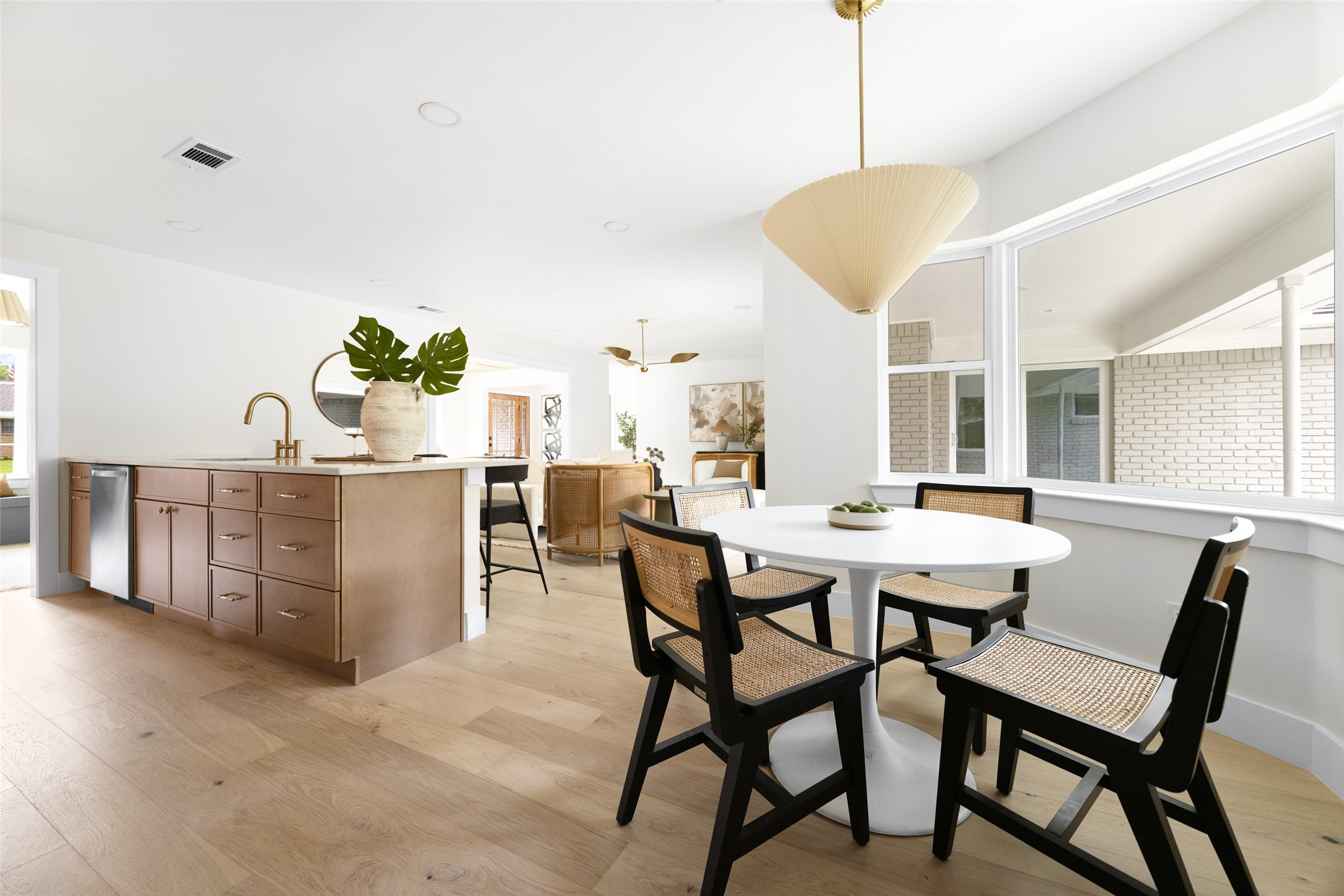 Open kitchen and dining area with a wood-paneled island and woven chairs around a white table.