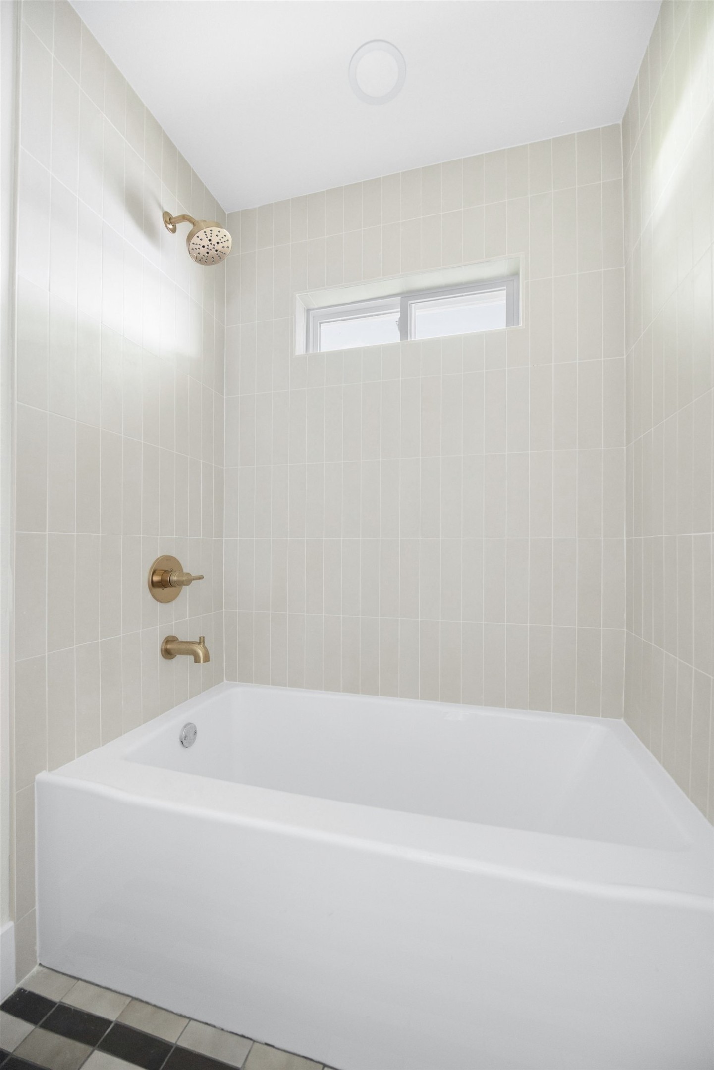 Bathroom bathtub with pale tile, brass shower fixtures, and a narrow window.