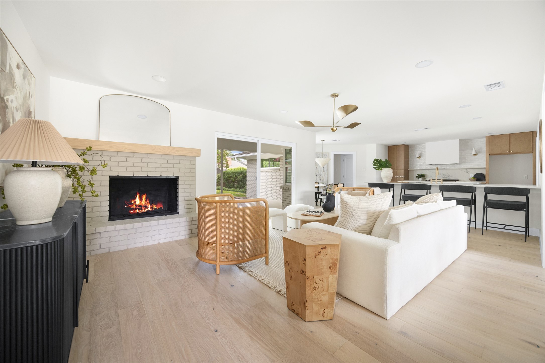 Open-plan living room and kitchen with a white brick fireplace, white sofas, and a kitchen island.