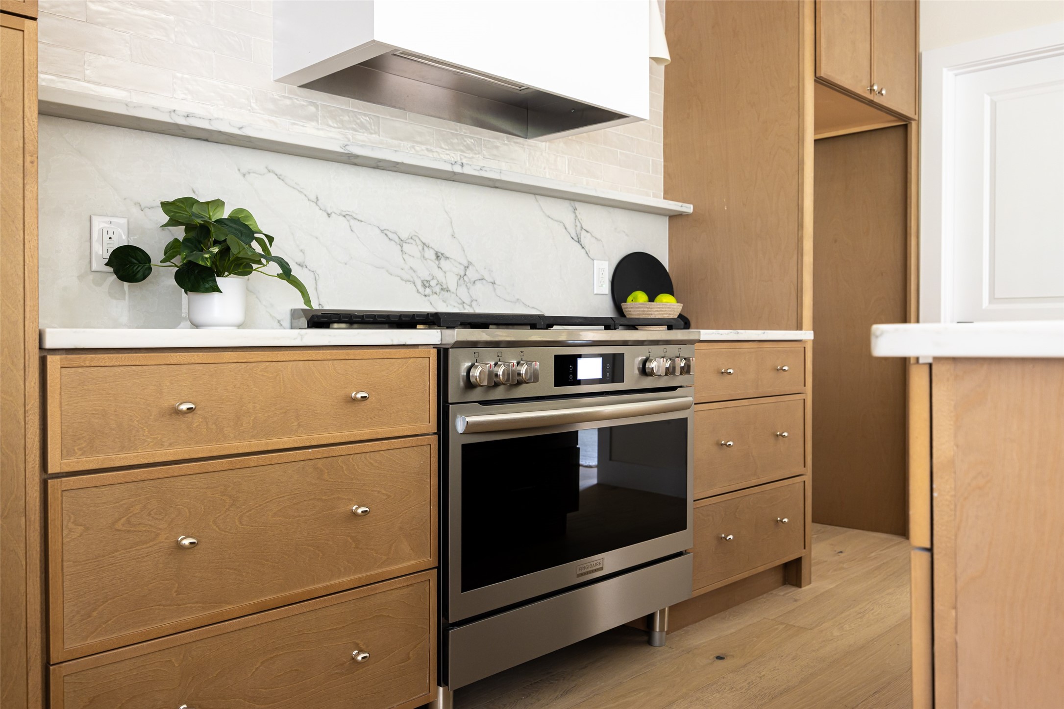 Kitchen range and oven set into warm wood cabinetry beneath a veined marble backsplash.