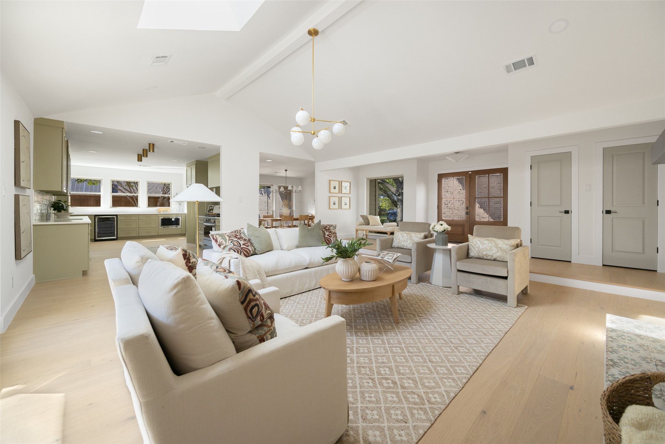 Staged living room with cream seating, a patterned rug, and an adjoining pale green kitchen.