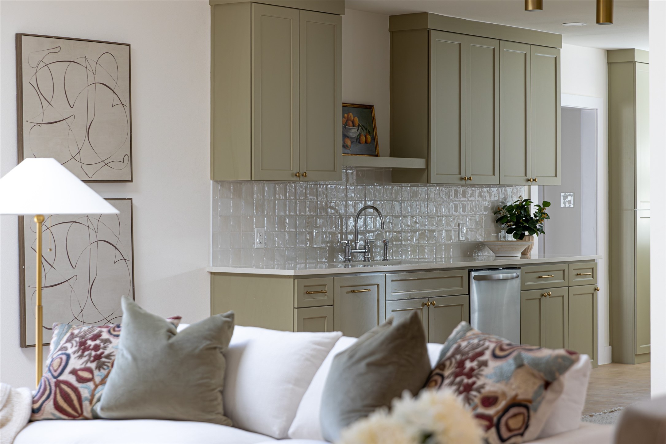 Kitchen with olive cabinetry, glossy tile backsplash, brass hardware, and a sofa in the foreground.