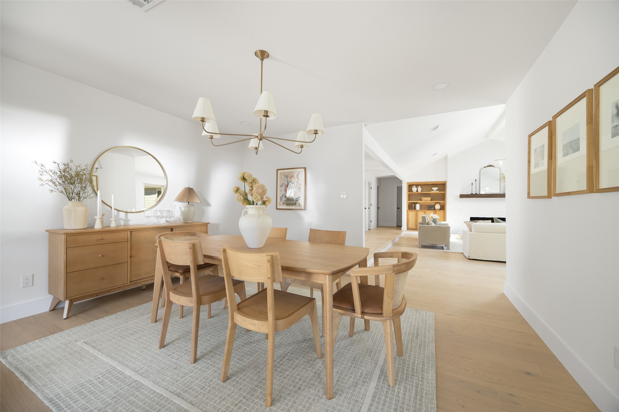 Dining room with a light wood table, round mirror, and an open view to the living room.