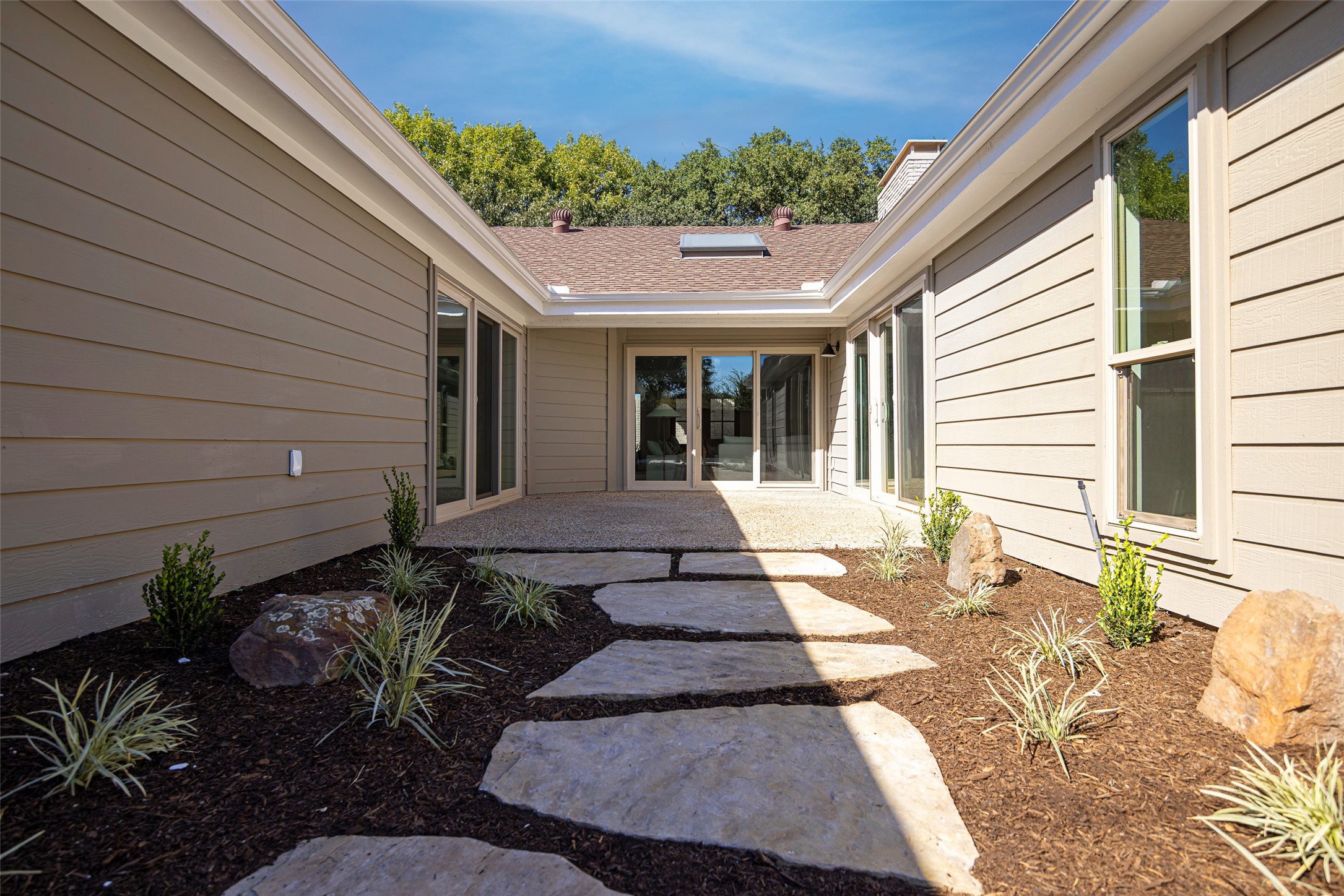 Enclosed courtyard with stone stepping pads, mulched landscaping, and glass doors.