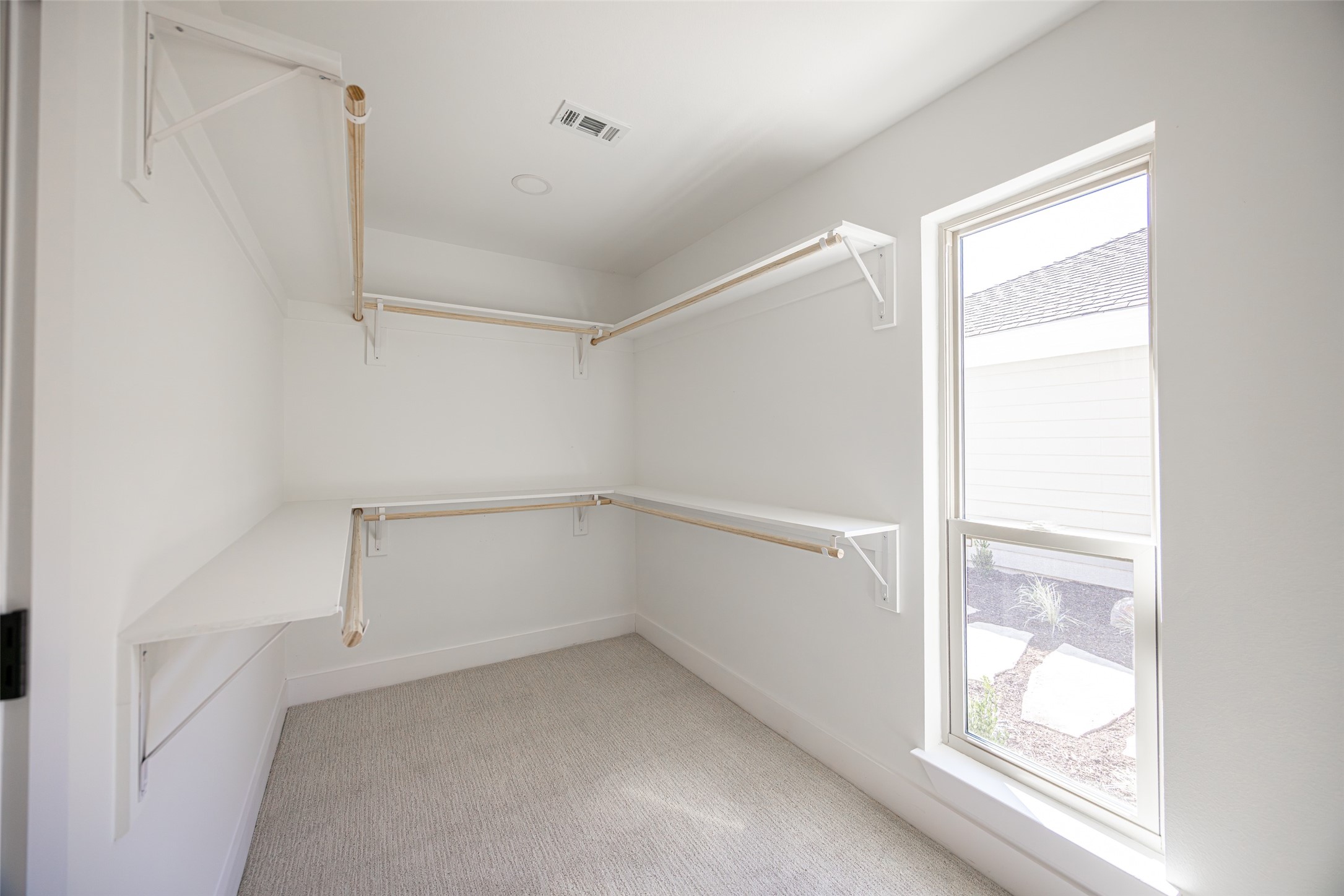 Walk-in closet with built-in shelves and hanging rods, beige carpet, and a tall window.