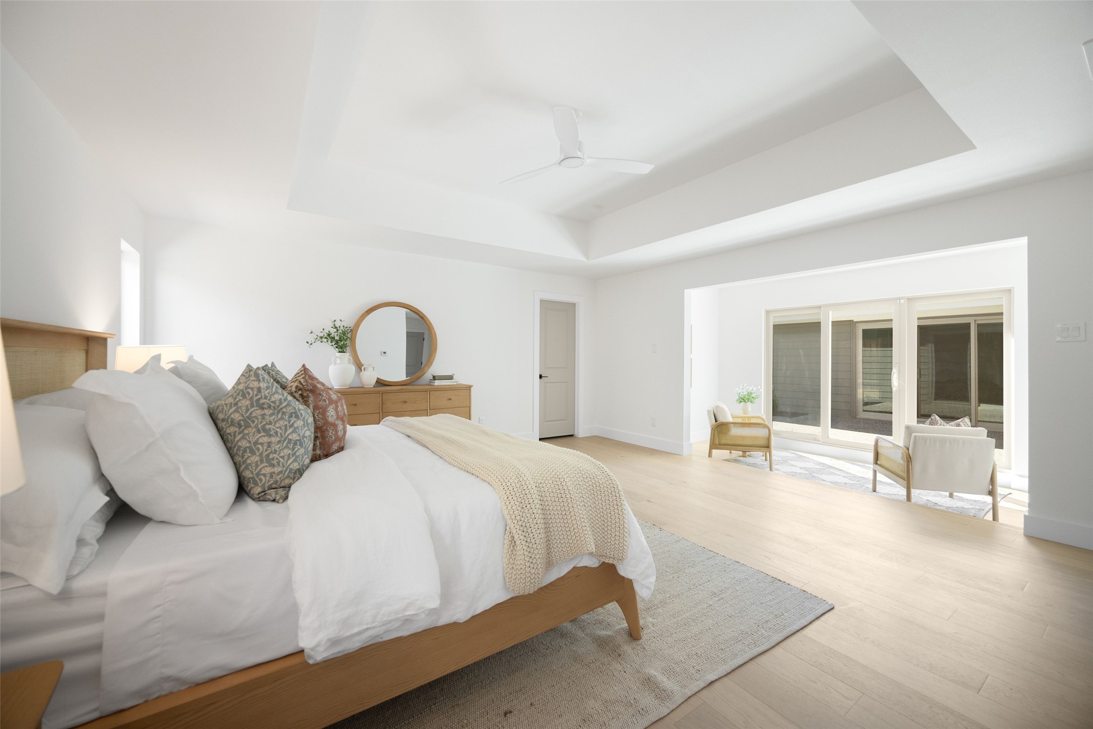 Staged bedroom with white bedding, a round mirror, and sliding glass doors to a patio.
