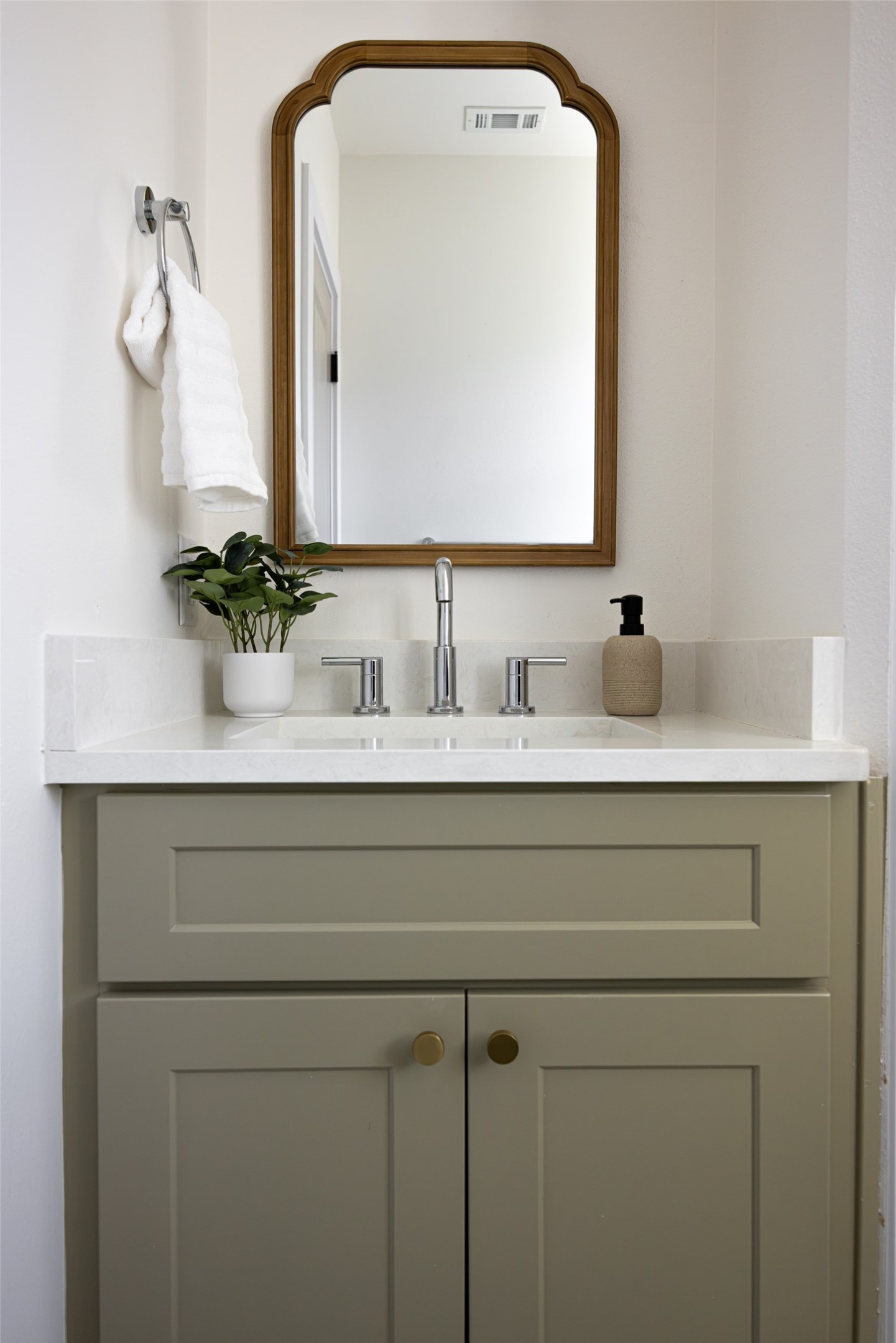 Bathroom vanity with sage-green cabinets, white countertop, chrome faucet, and wood-framed mirror.
