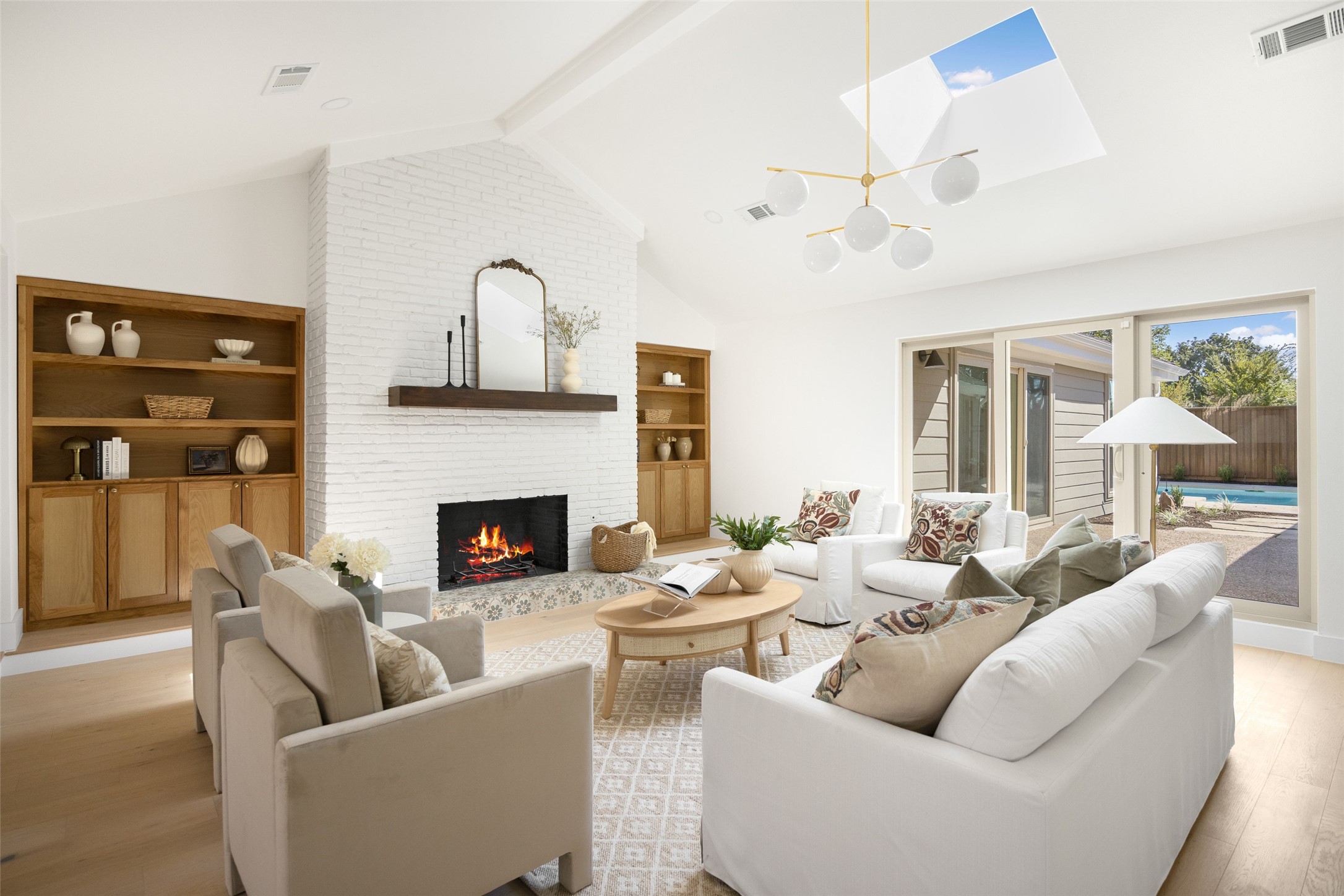 Living room with a white brick fireplace, built-in wood shelves, and sliding doors overlooking a pool.