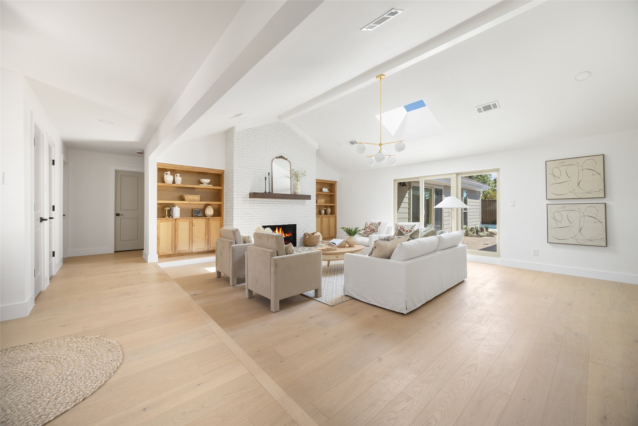 Staged living room with a white brick fireplace, wood built-ins, pale floors, and sliding patio doors.