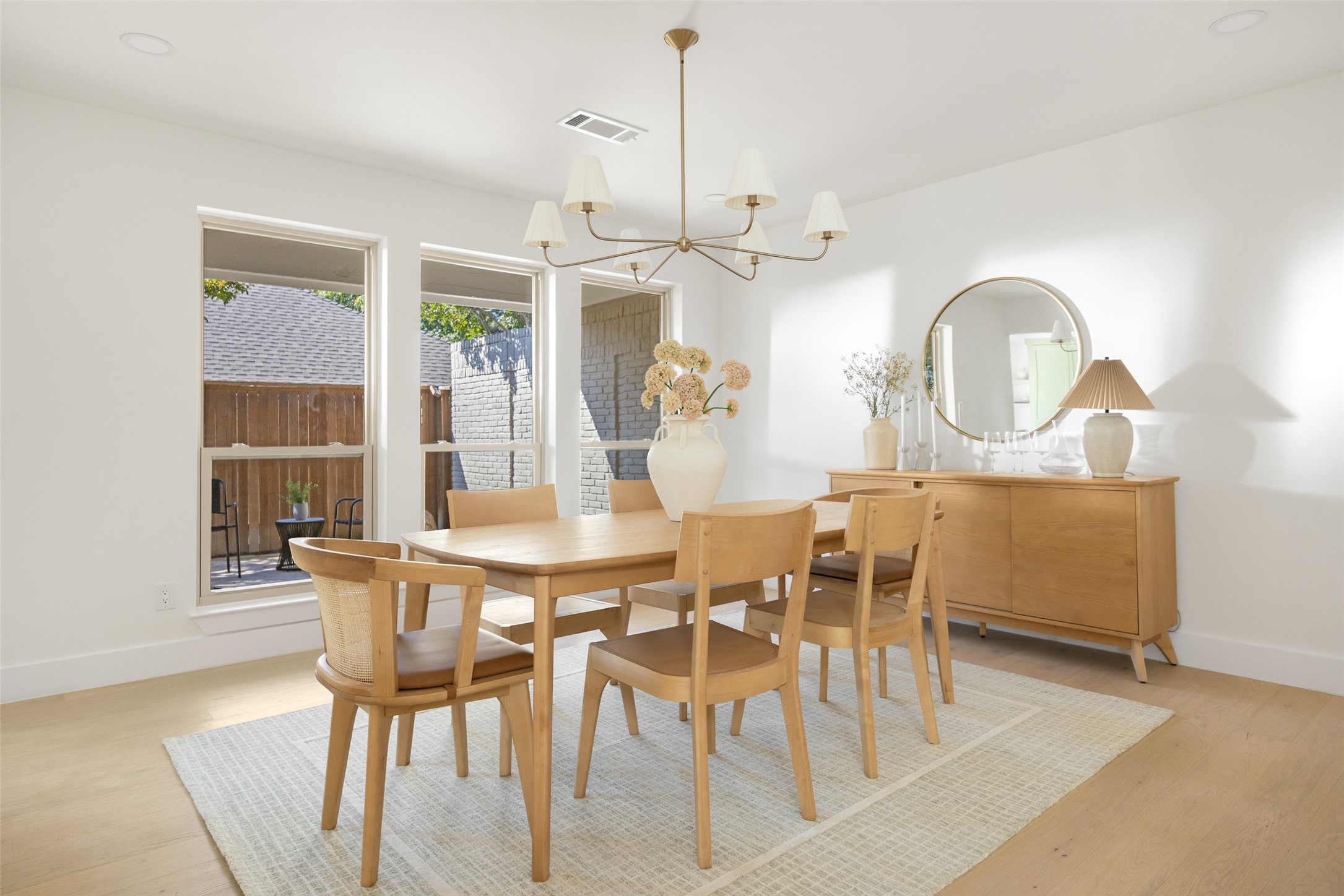 Bright dining room with a light wood table, brass chandelier, and tall windows.