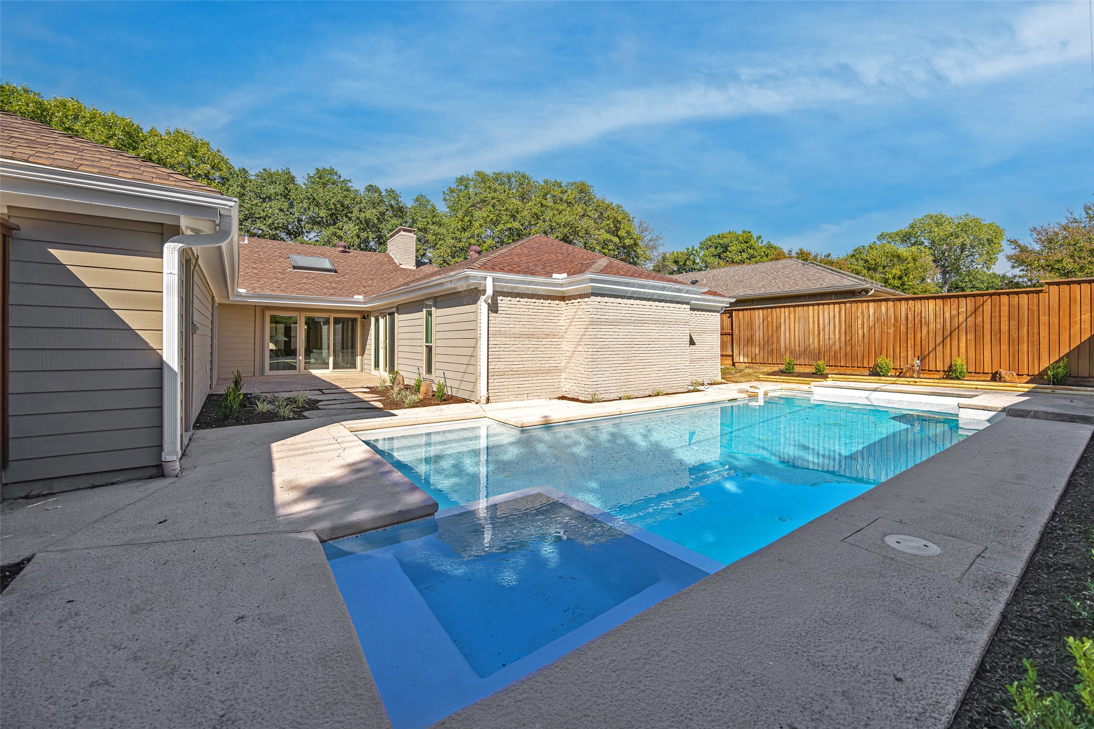 Backyard swimming pool with a broad concrete deck beside the home and a tall wooden privacy fence.